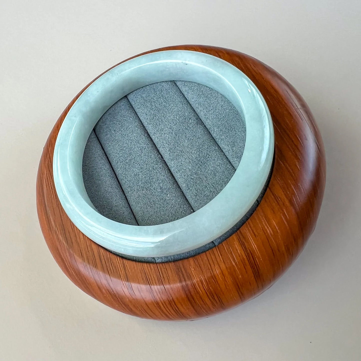 Angled view of polished light blue jade bangle resting in a wood display case