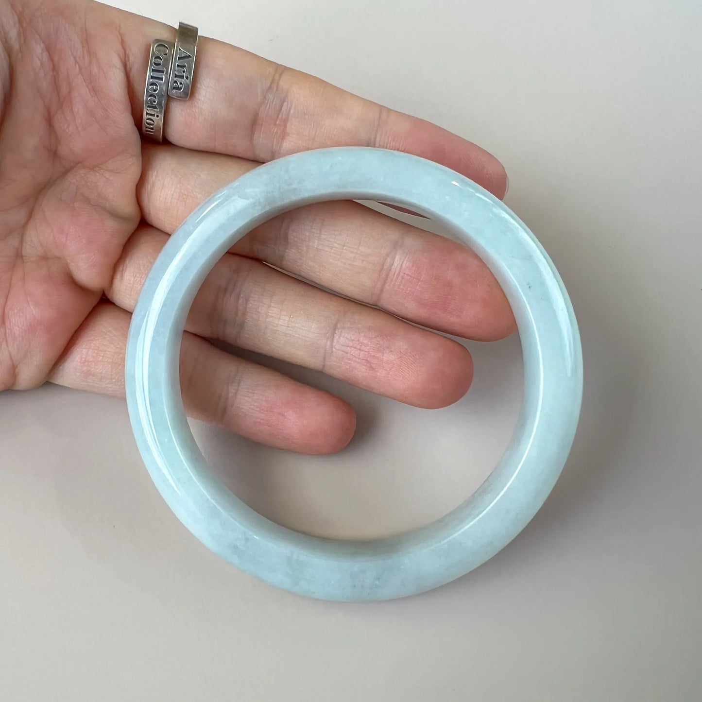 Handheld front view of glossy light blue jade bangle showing rounded profile