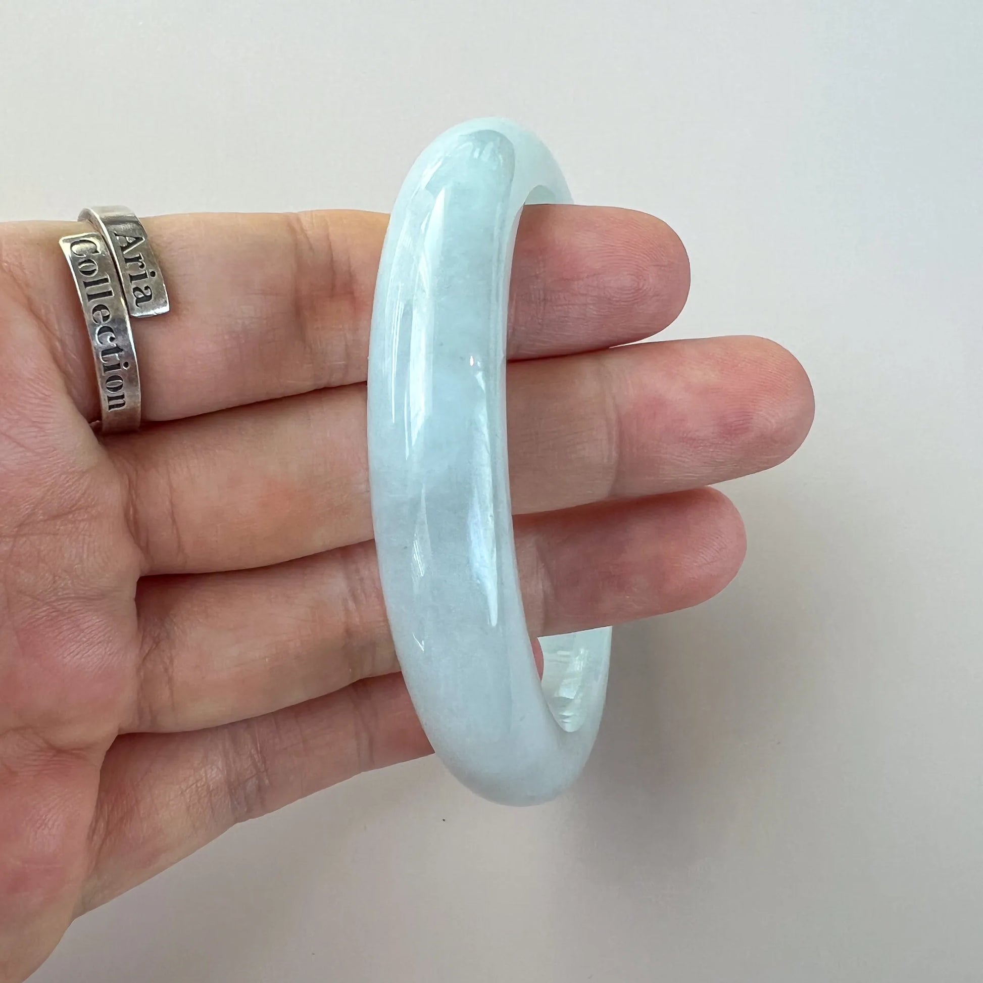 Side view of polished pale blue jade bangle held between fingers against white background