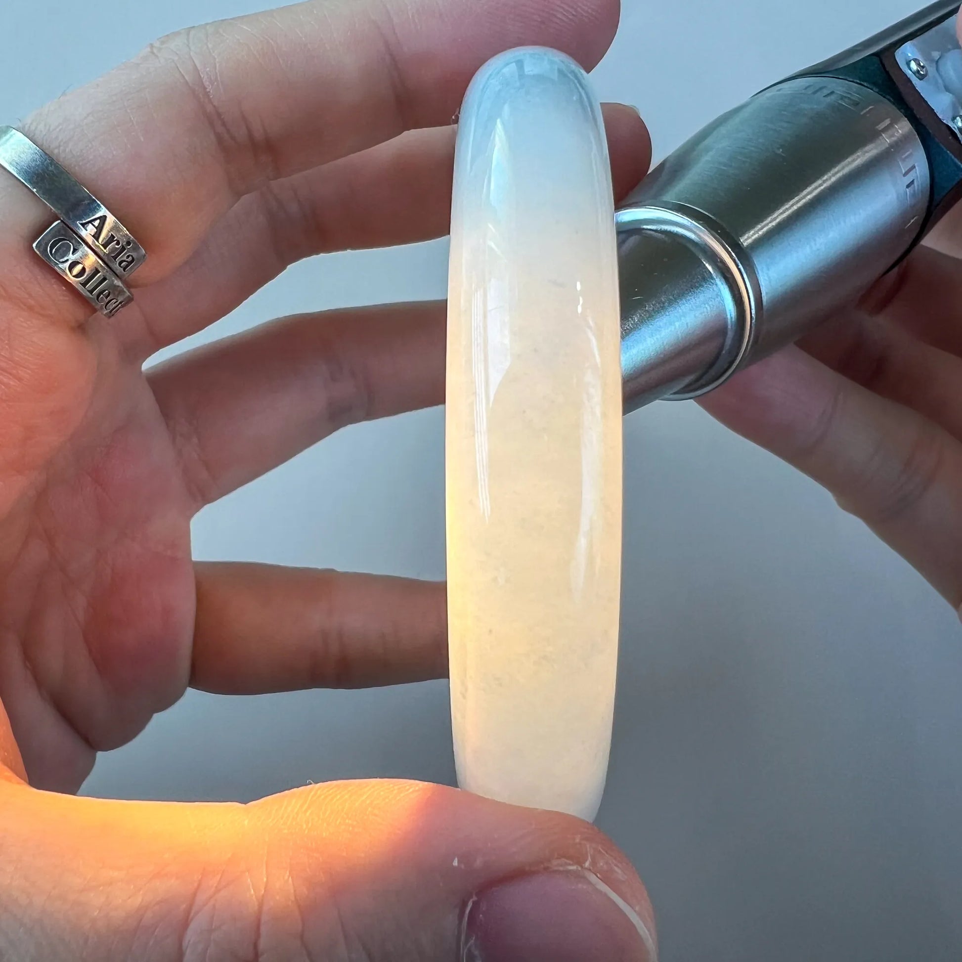 Side view of translucent jade bangle under flashlight, showing creamy color and polish