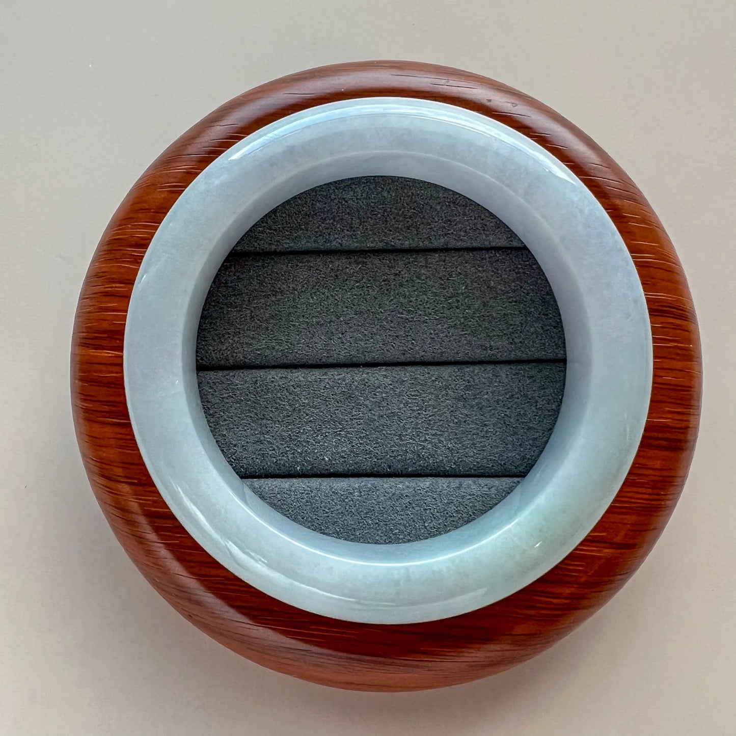 Top view of light blue jade bangle on textured jewelry cushion with wood backdrop