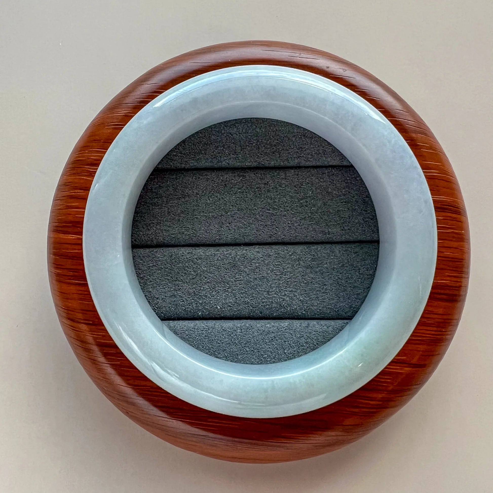 Top view of light blue jade bangle on textured jewelry cushion with wood backdrop