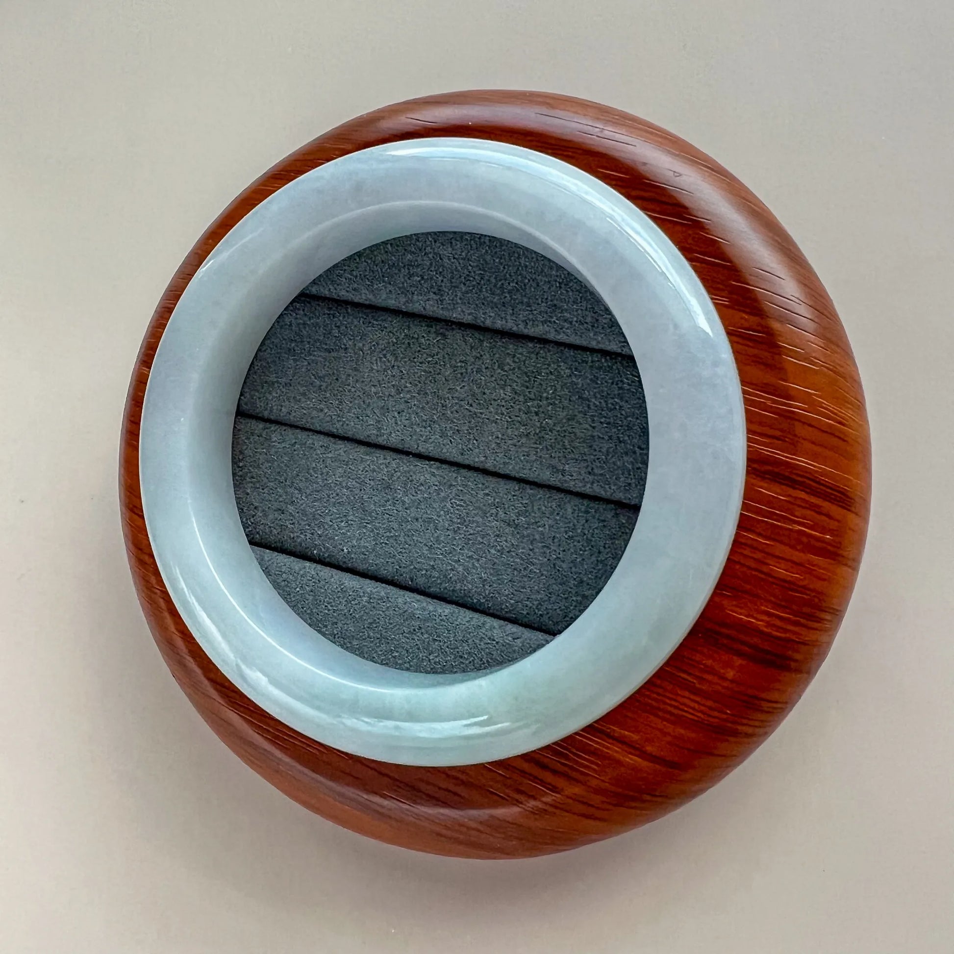 Angled view of polished pale blue jade bangle with rich wood-toned display stand
