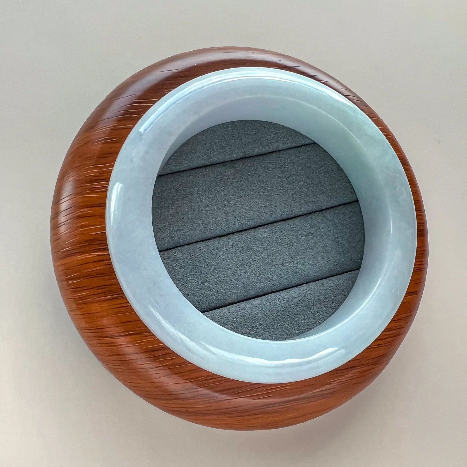 Round overhead view of smooth light blue jade bangle against a dark cushion insert