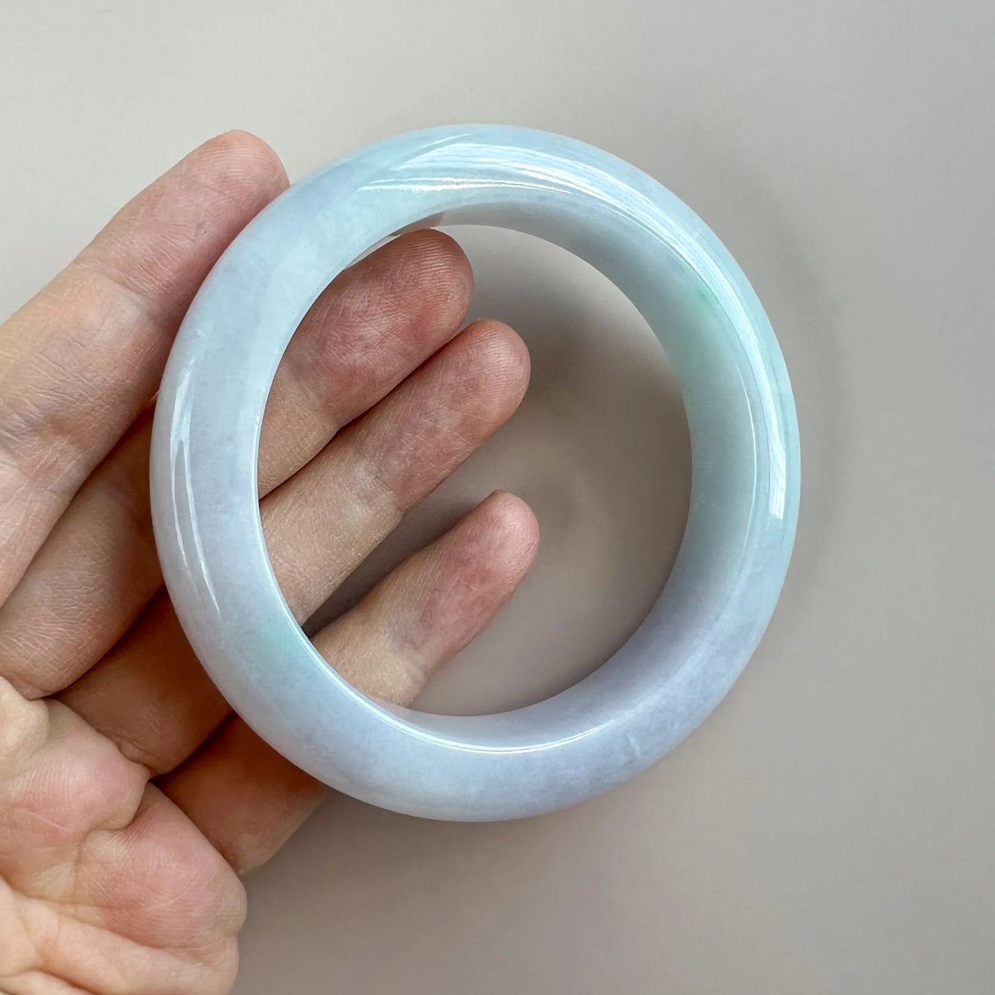 Handheld view of glossy pale blue jade bangle showing rounded profile and translucent finish