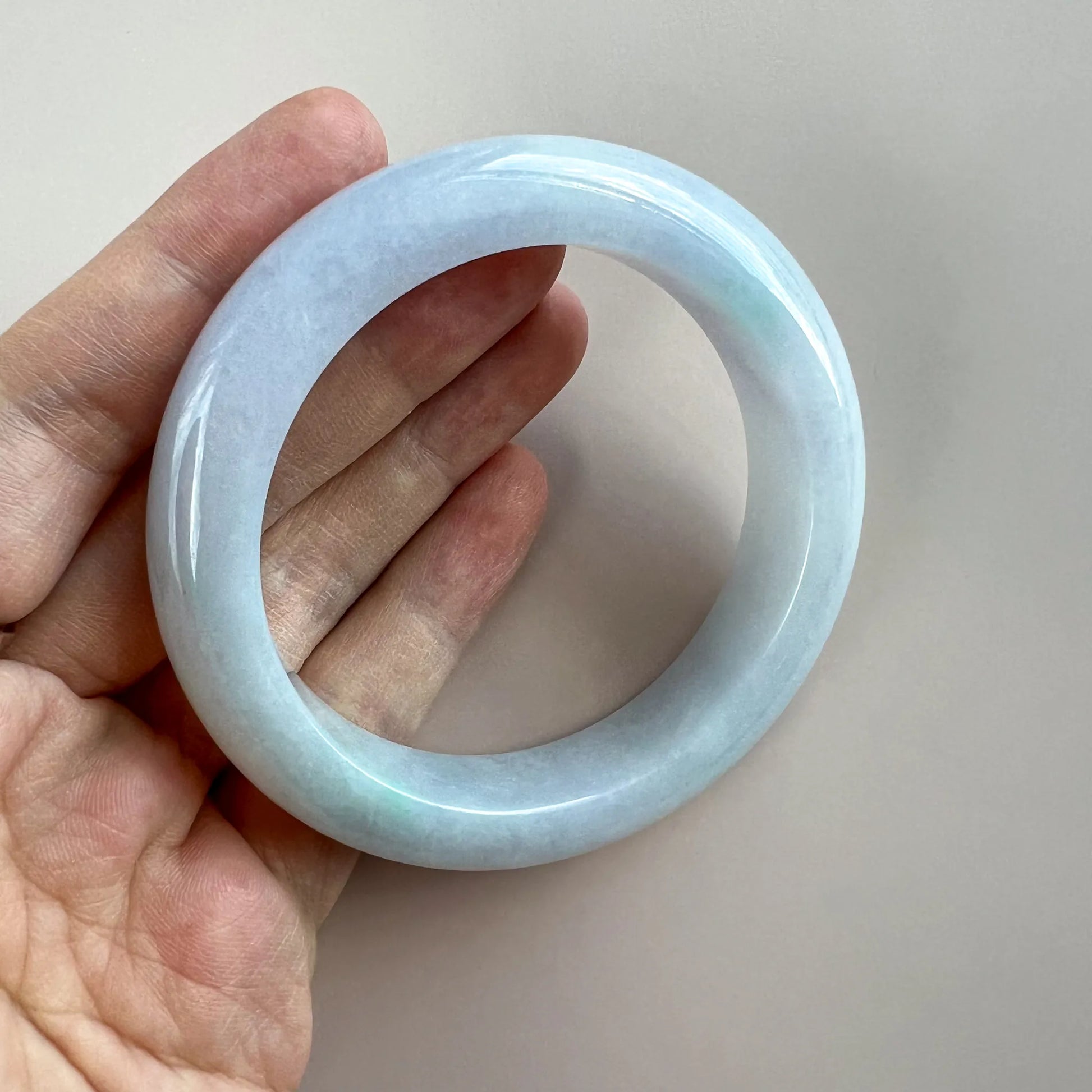 Handheld view of smooth light blue jade bangle with polished translucent surface