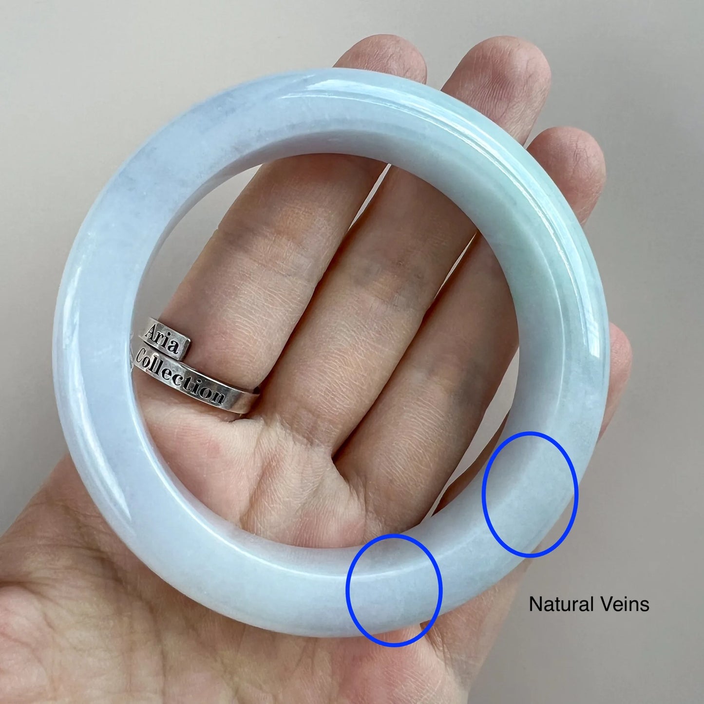 Handheld front view of pale blue jade bangle with natural veins marked on the surface