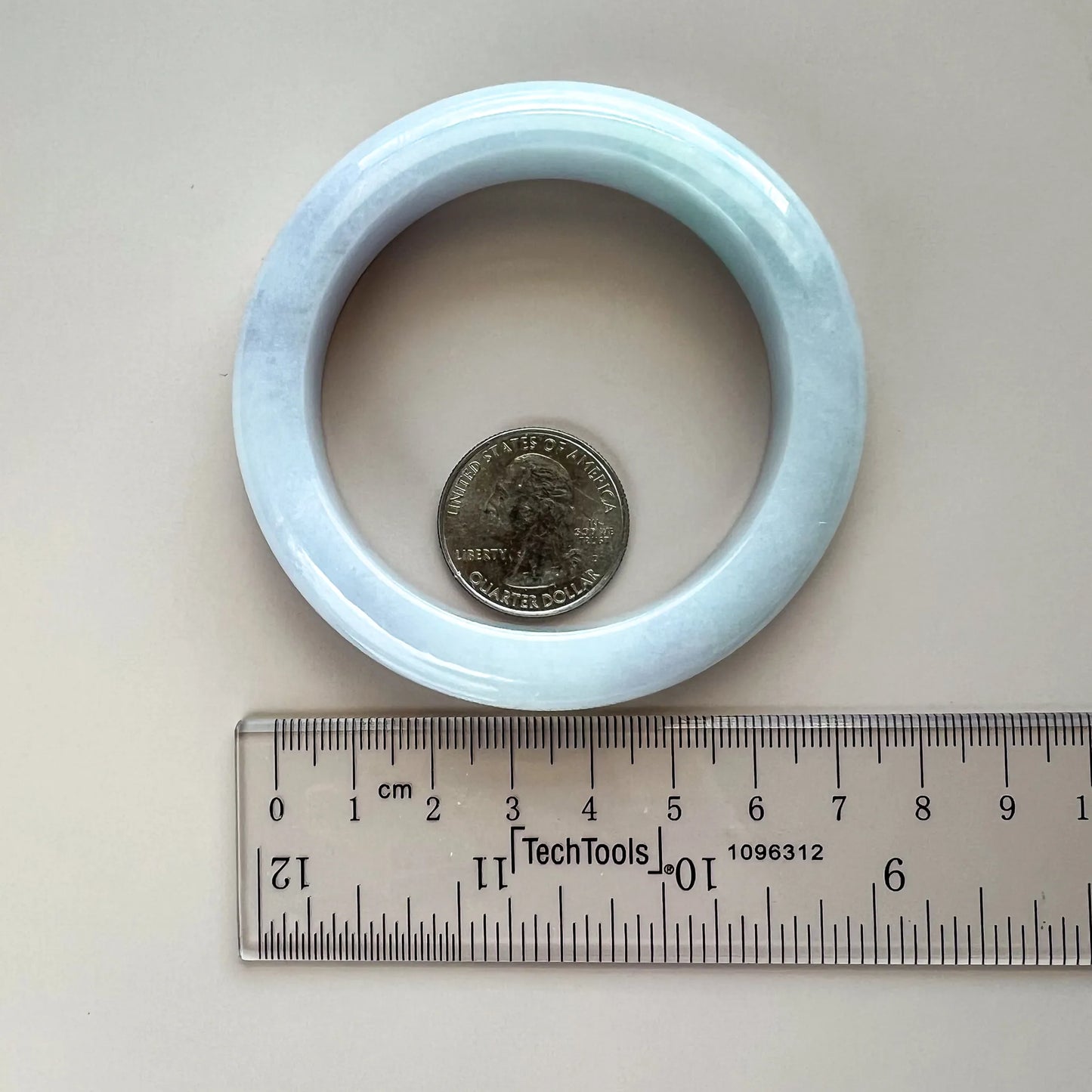 Light blue jadeite bangle shown with ruler and coin for interior diameter and scale