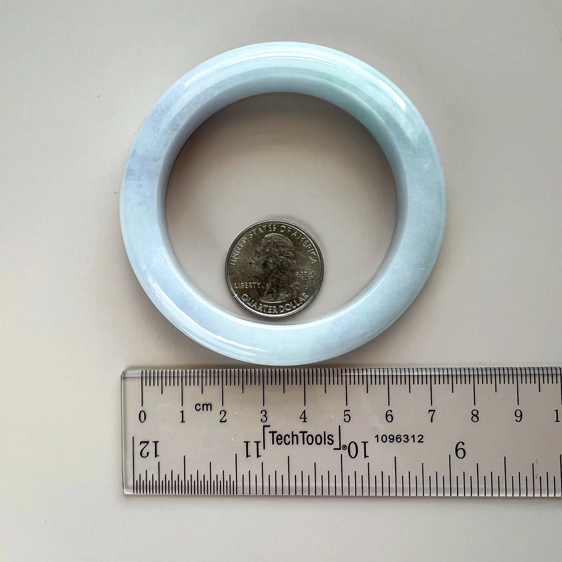Light blue jadeite bangle shown with ruler and coin for interior diameter and scale