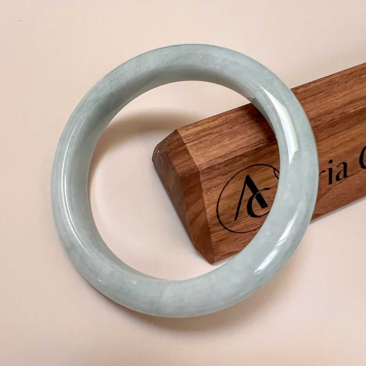 Front view of smooth pale green jade bangle with glossy finish on display stand