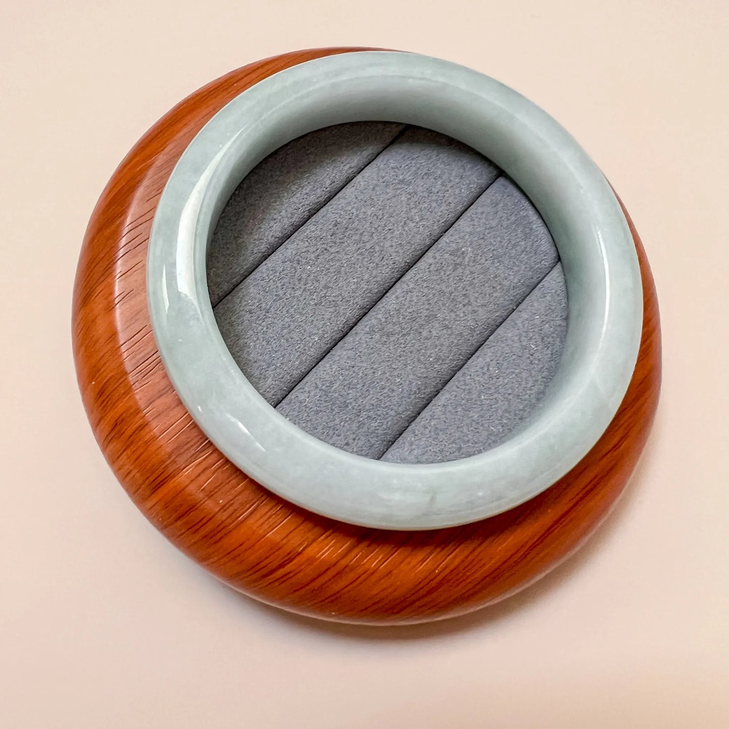 Angled overhead view of jade bangle resting on cushioned wooden stand