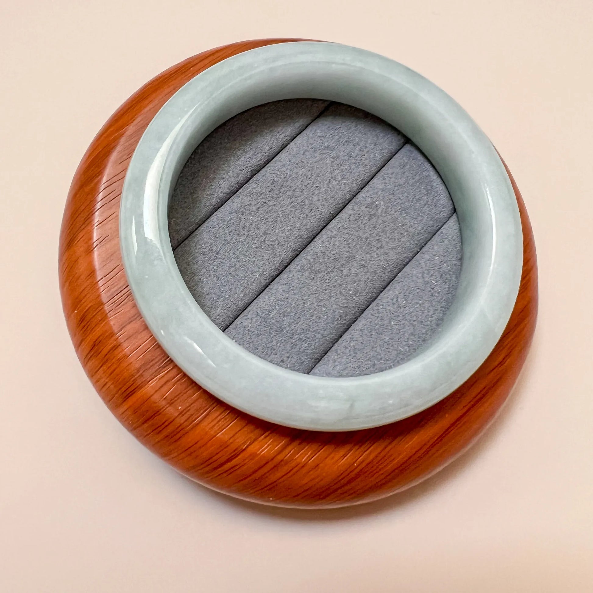 Angled overhead view of jade bangle resting on cushioned wooden stand