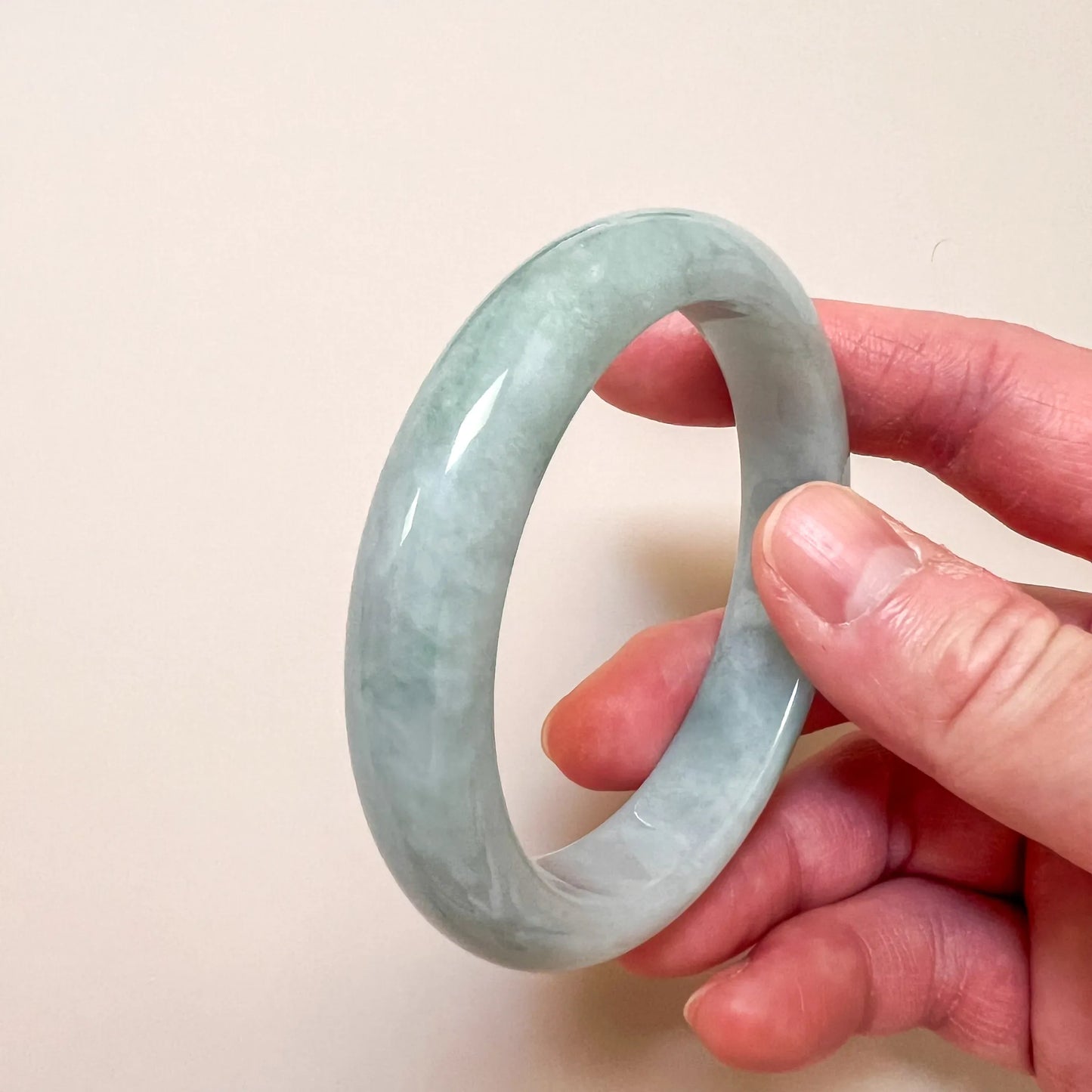 Side angled view of glossy pale green jade bangle held between fingers