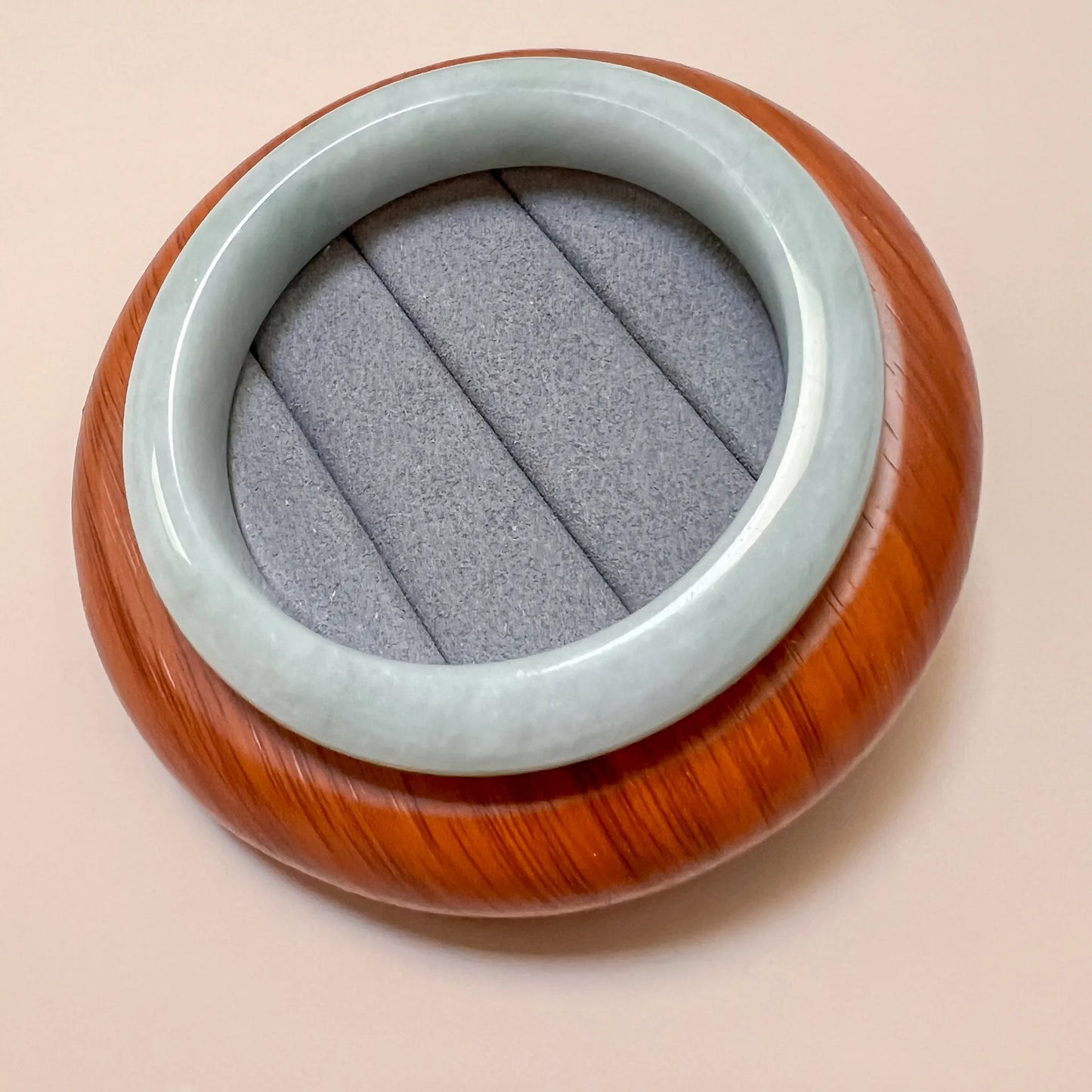 Top-down view of light green gray jadeite bangle with glossy polished finish and wood display stand