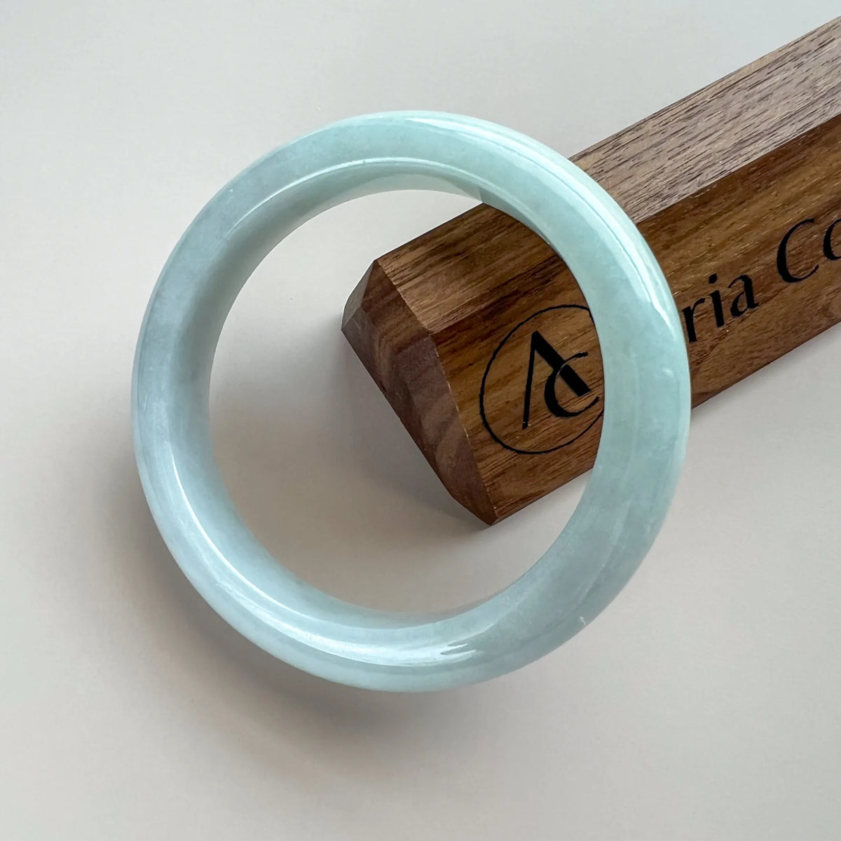 Glossy pale blue jade bangle angled beside a wooden display block on a light background