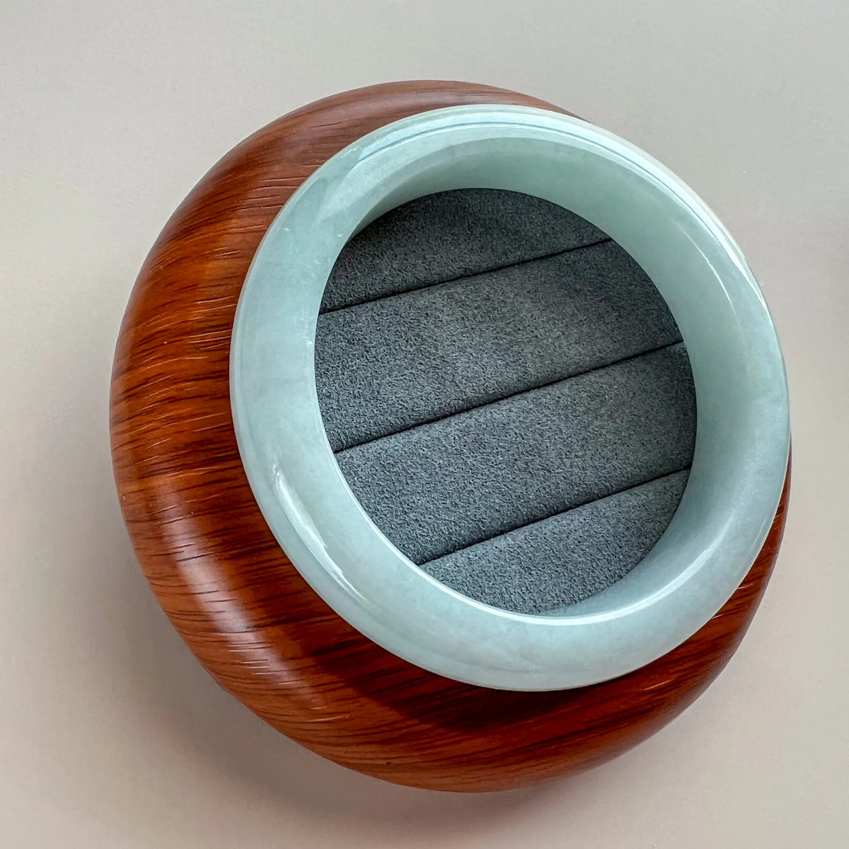 Angled top view of polished pale blue jade bangle resting on a wooden display base
