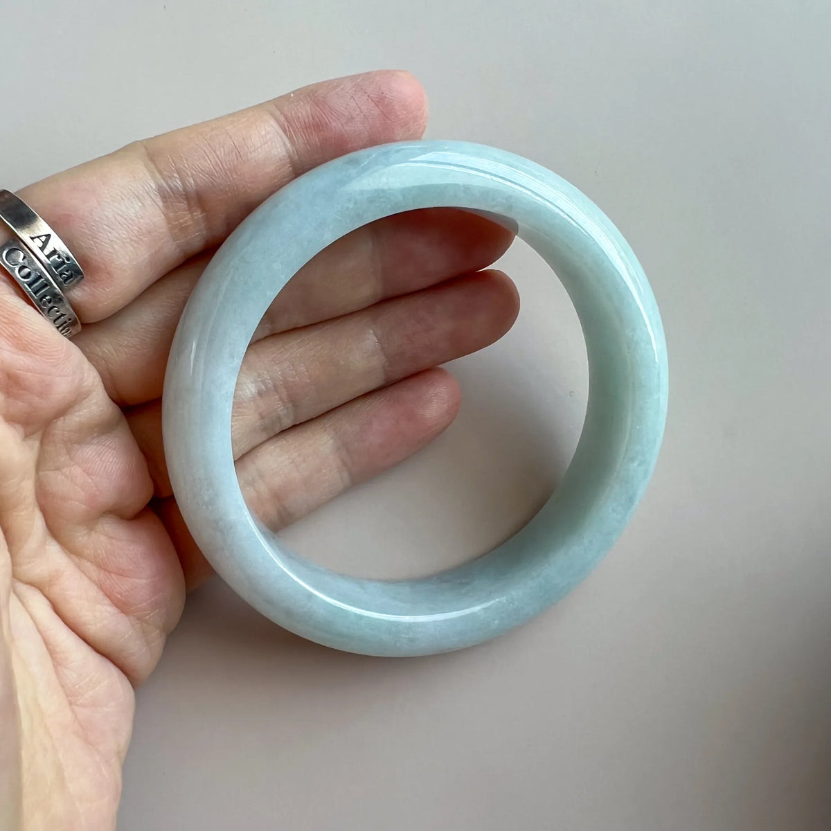 Hand-held view of the light blue jadeite bangle showing its rounded profile, translucency, and glossy surface