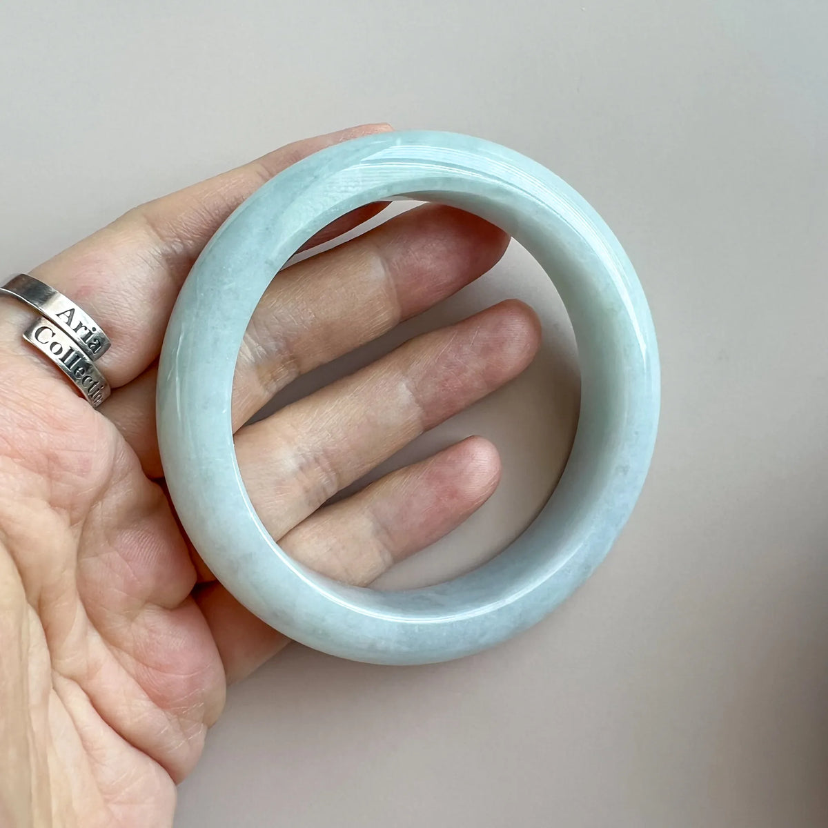Close hand-held view of polished pale blue jade bangle with smooth rounded surface