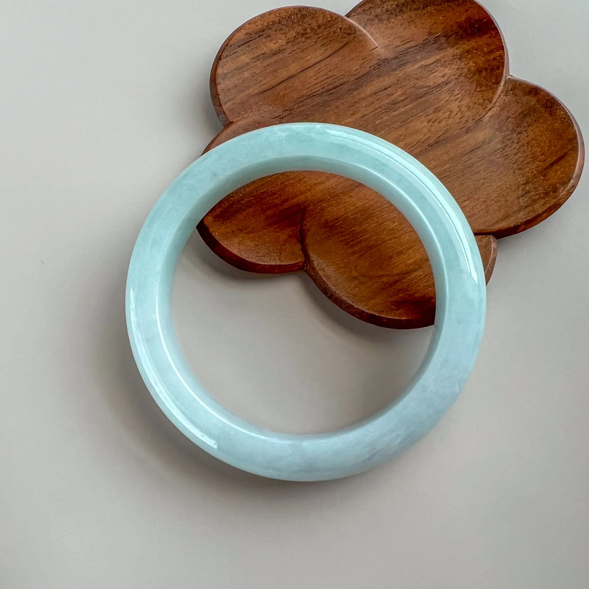 Glossy pale blue jade bangle on a carved wooden stand, shown front view with smooth finish