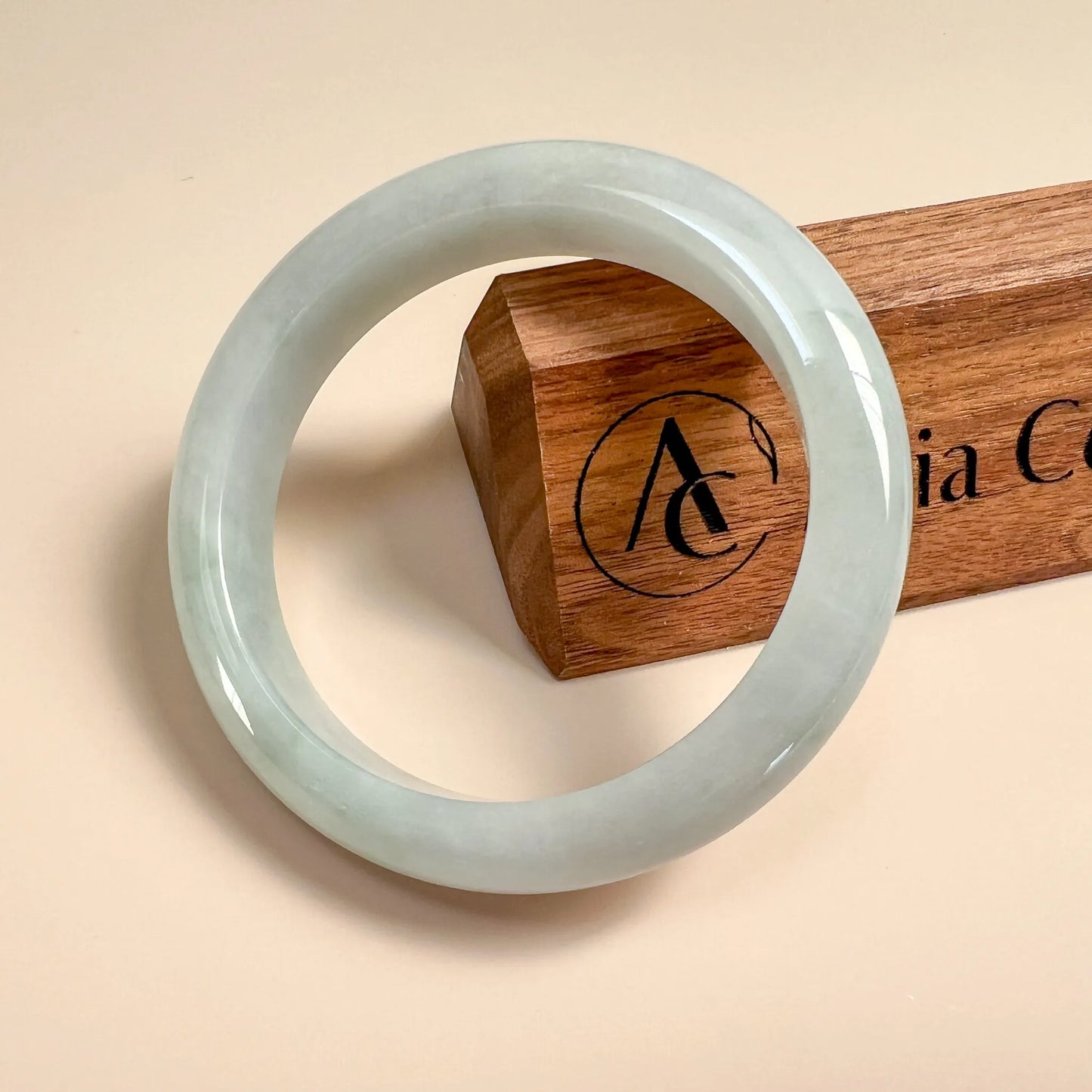 Front view of pale green jade bangle with smooth polished finish on beige background