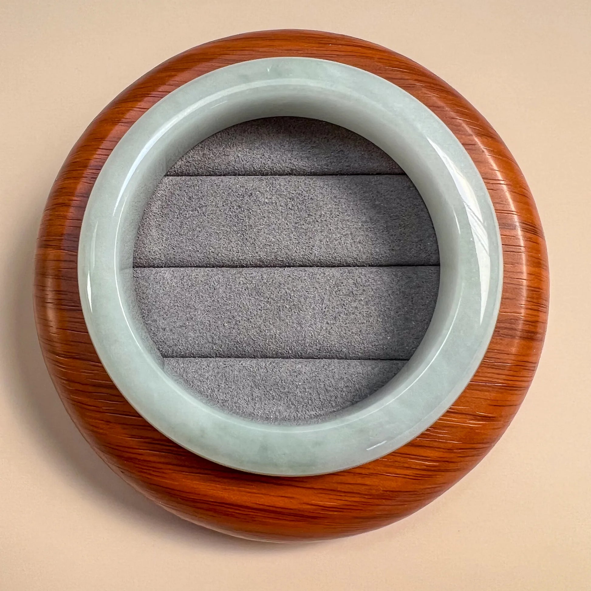 Top view of jade bangle resting on round wood display stand with grey insert