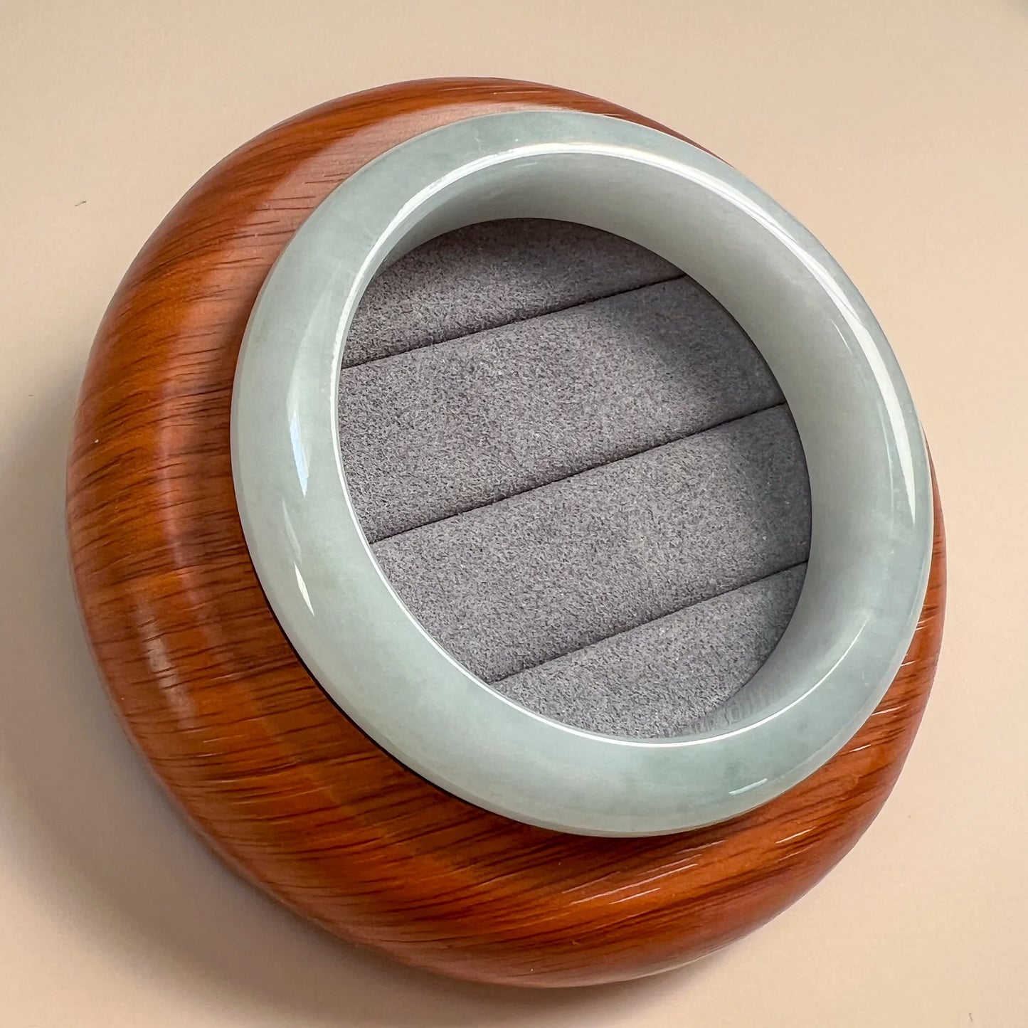 Angled view of polished jade bangle on wood display stand showing round profile