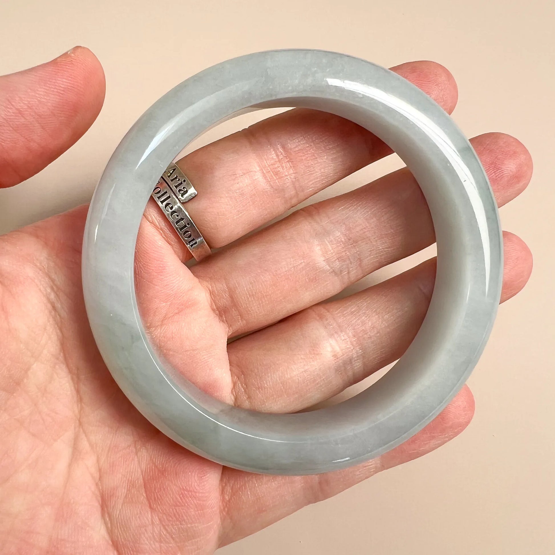 Jade bangle held in hand, showing glossy translucent finish and smooth rounded edge
