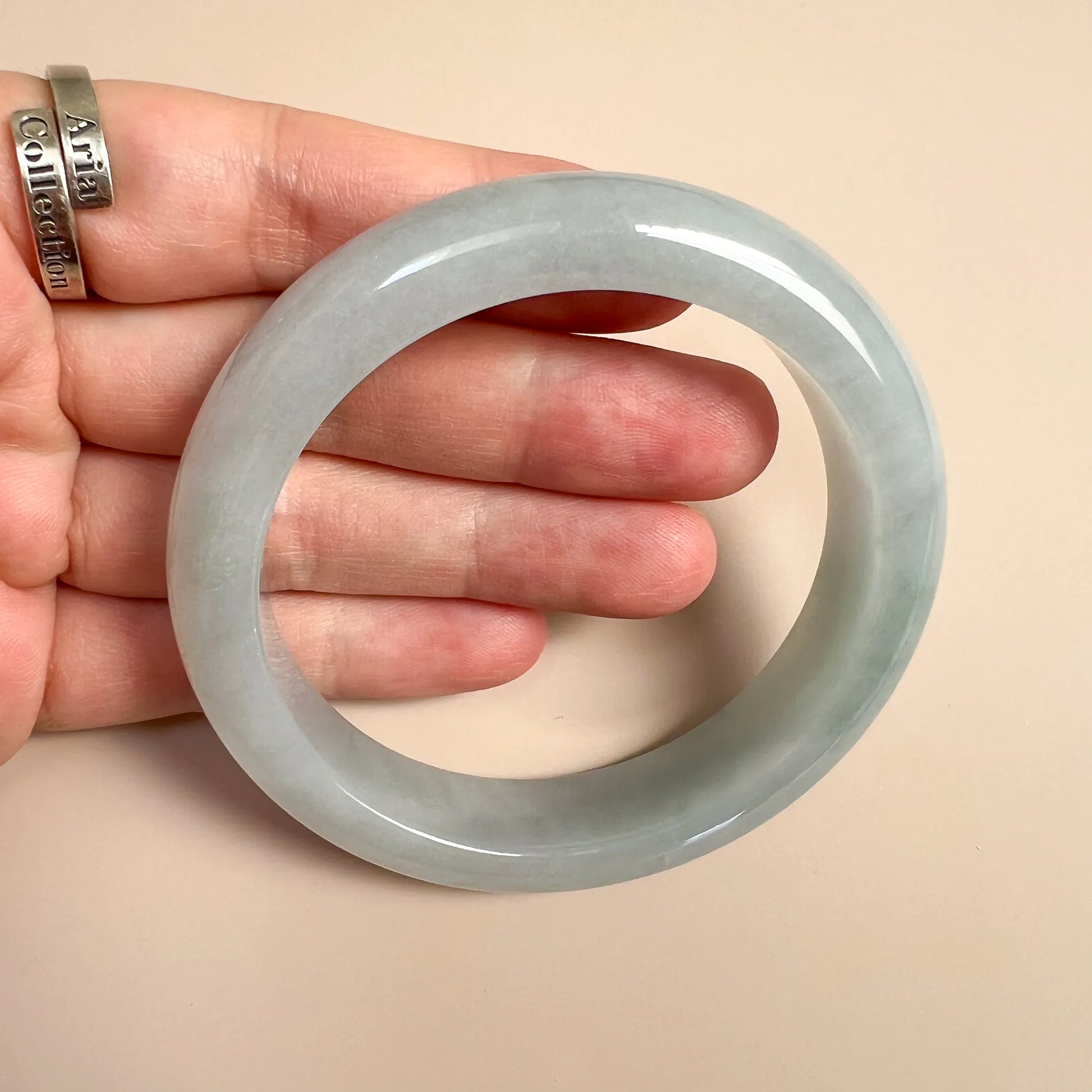 Side view of pale green jade bangle in hand with polished surface and oval profile