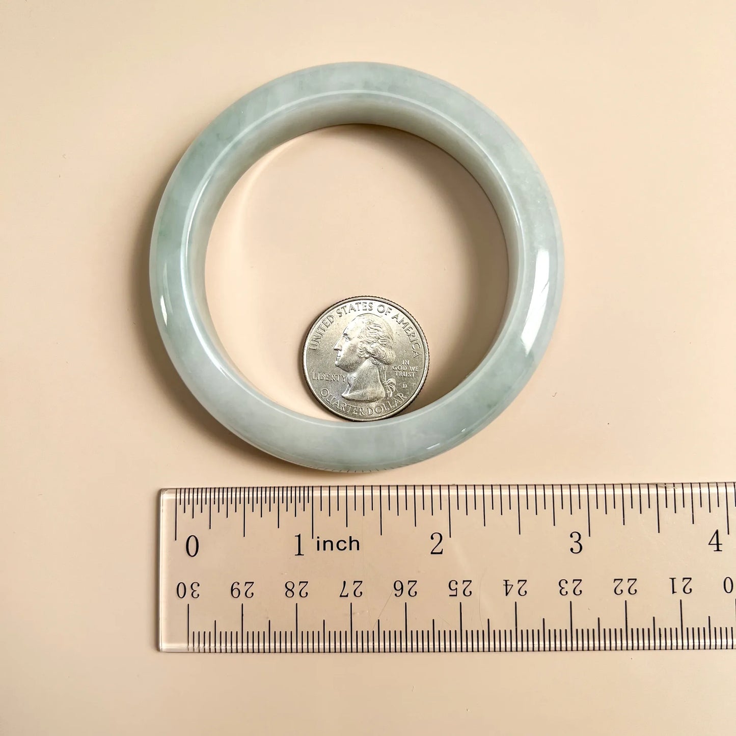 Light green-blue jadeite bangle shown with a quarter and ruler for scale