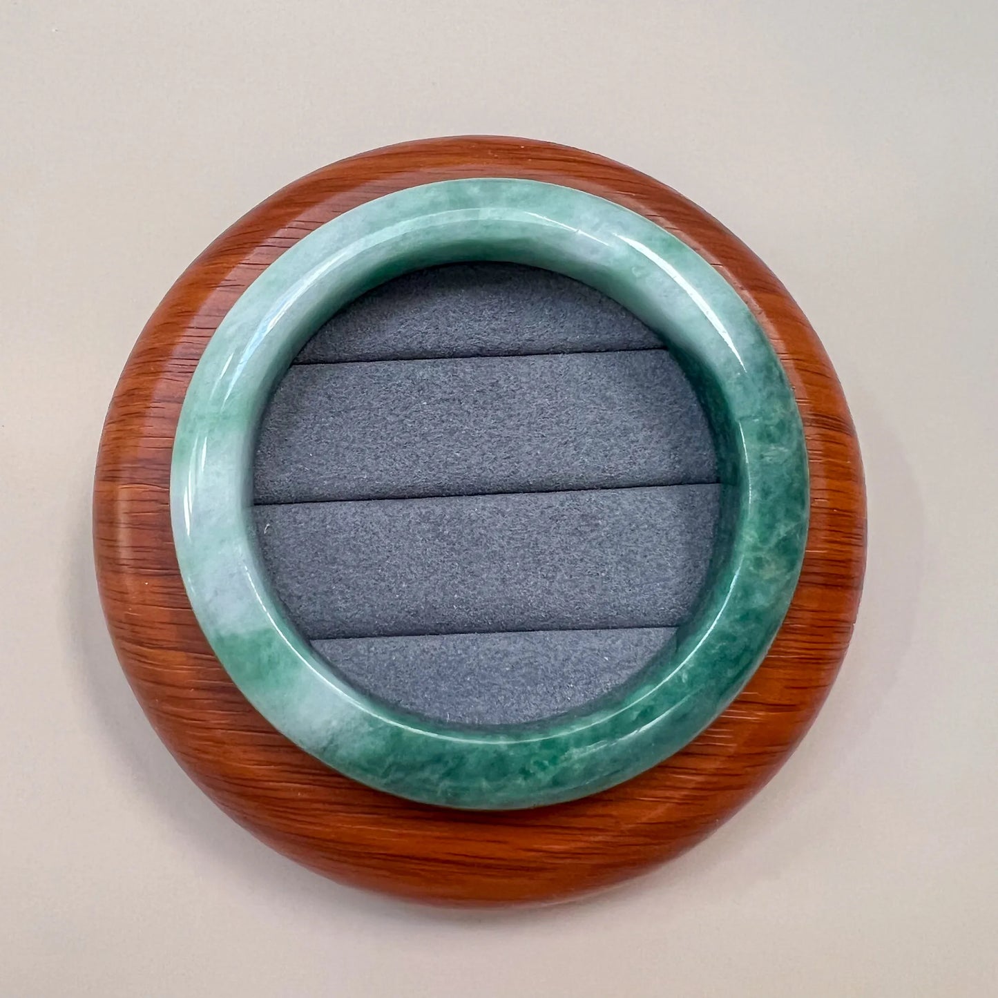 Top view of green jade bangle on a wooden display base with gray cushion insert