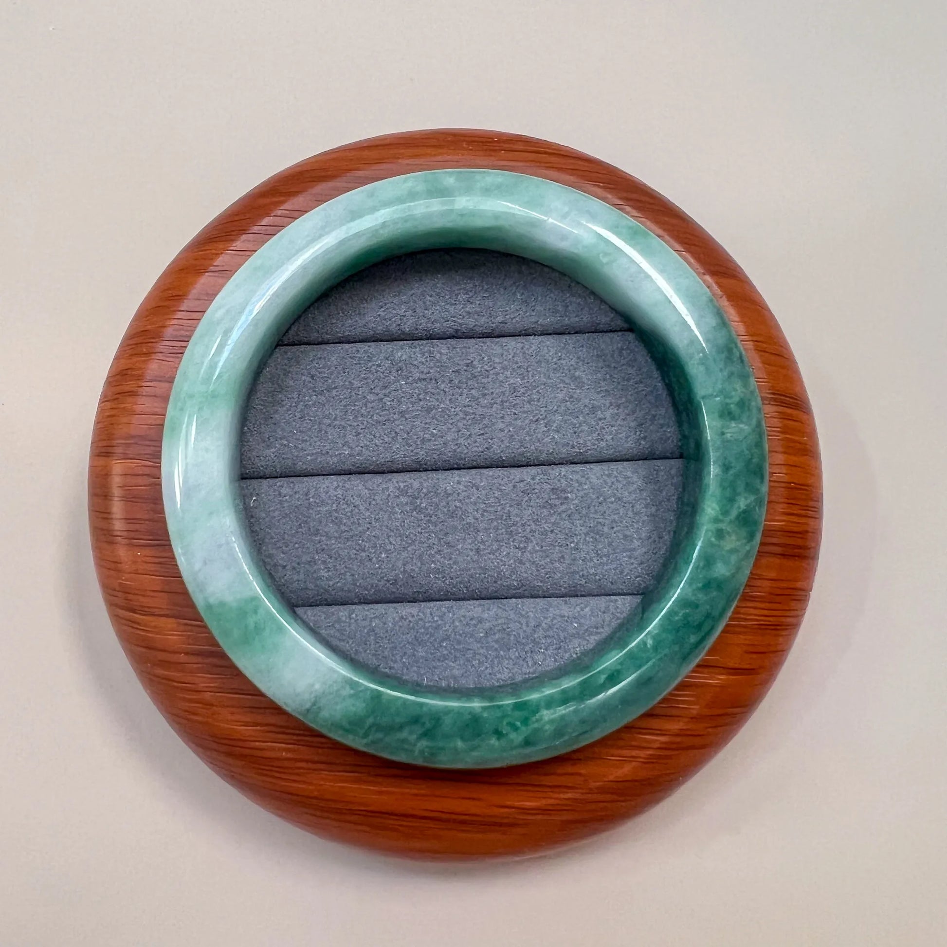 Top view of green jade bangle on a wooden display base with gray cushion insert