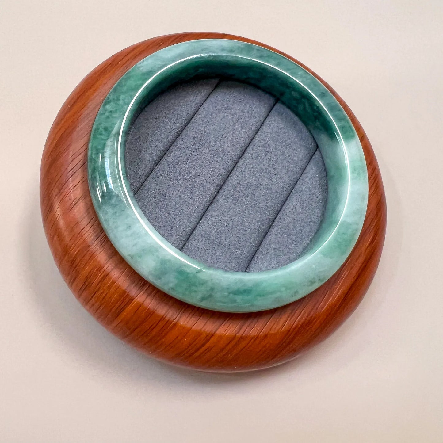 Angled top view of glossy green jade bangle on a round wooden display base