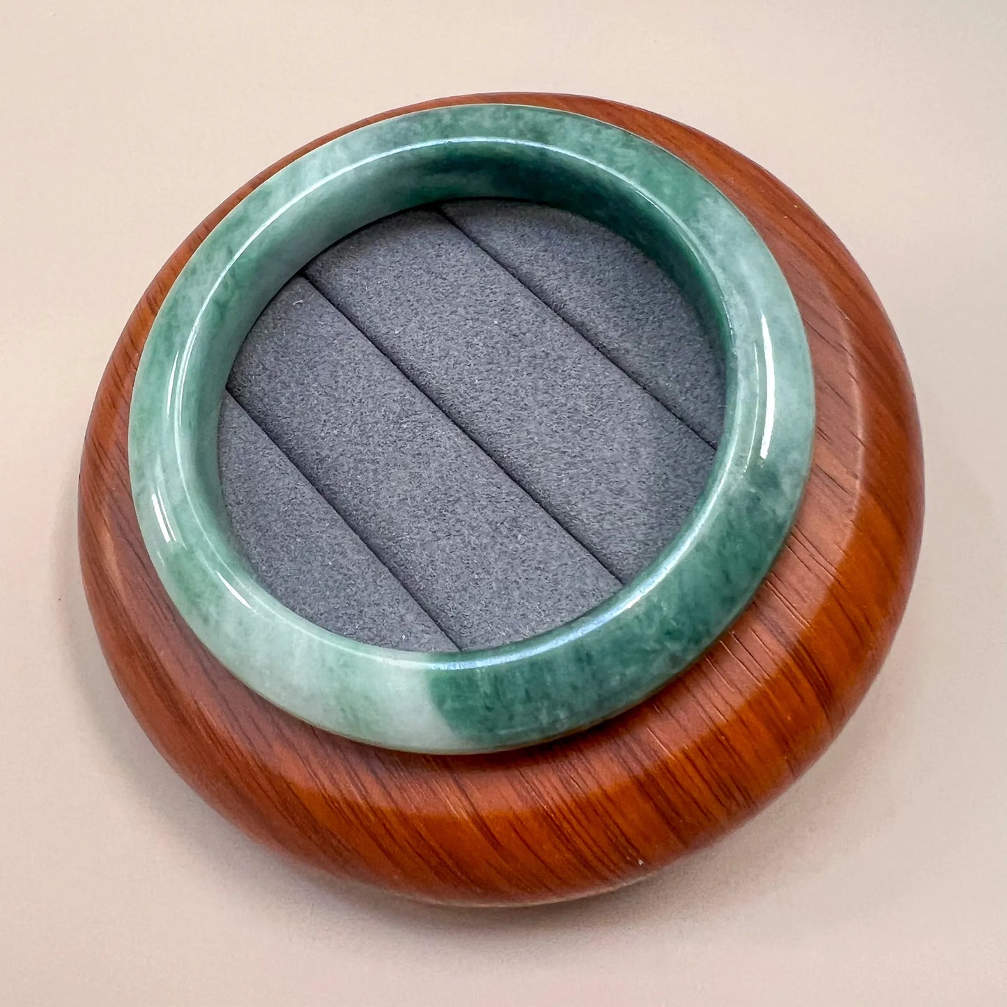 Angled view of green jade bangle with smooth polished finish on wooden display base