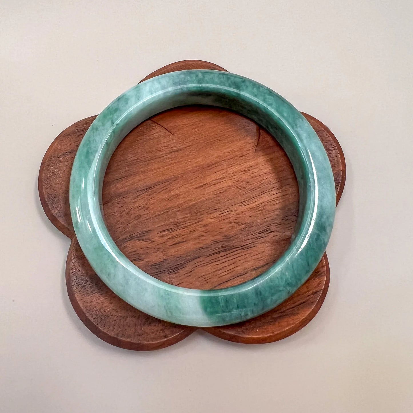 Green jade bangle centered on a flower-shaped wooden display base, polished finish