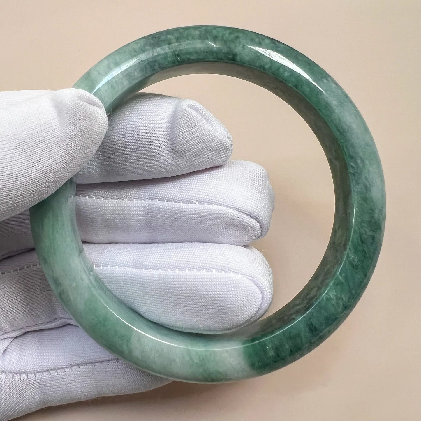 Handheld front view of translucent green jade bangle with smooth polished surface