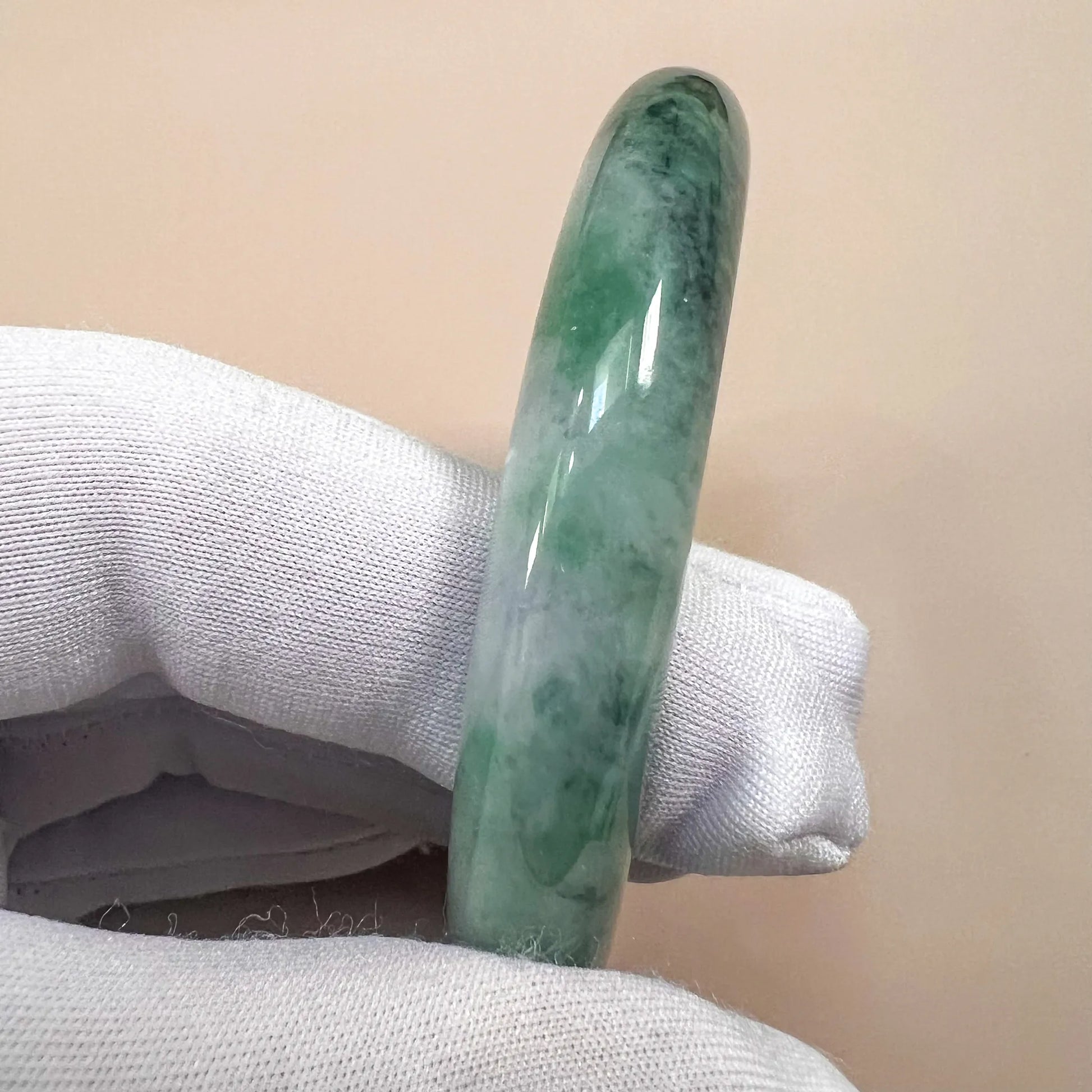Side profile of the green jadeite bangle showing its rounded form, mottled color, and glossy polish