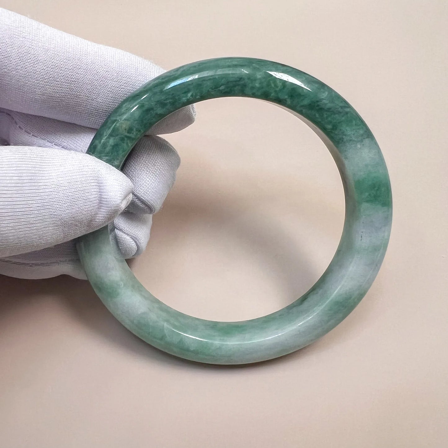 Handheld front view of green jade bangle showing marbled color variation and glossy finish