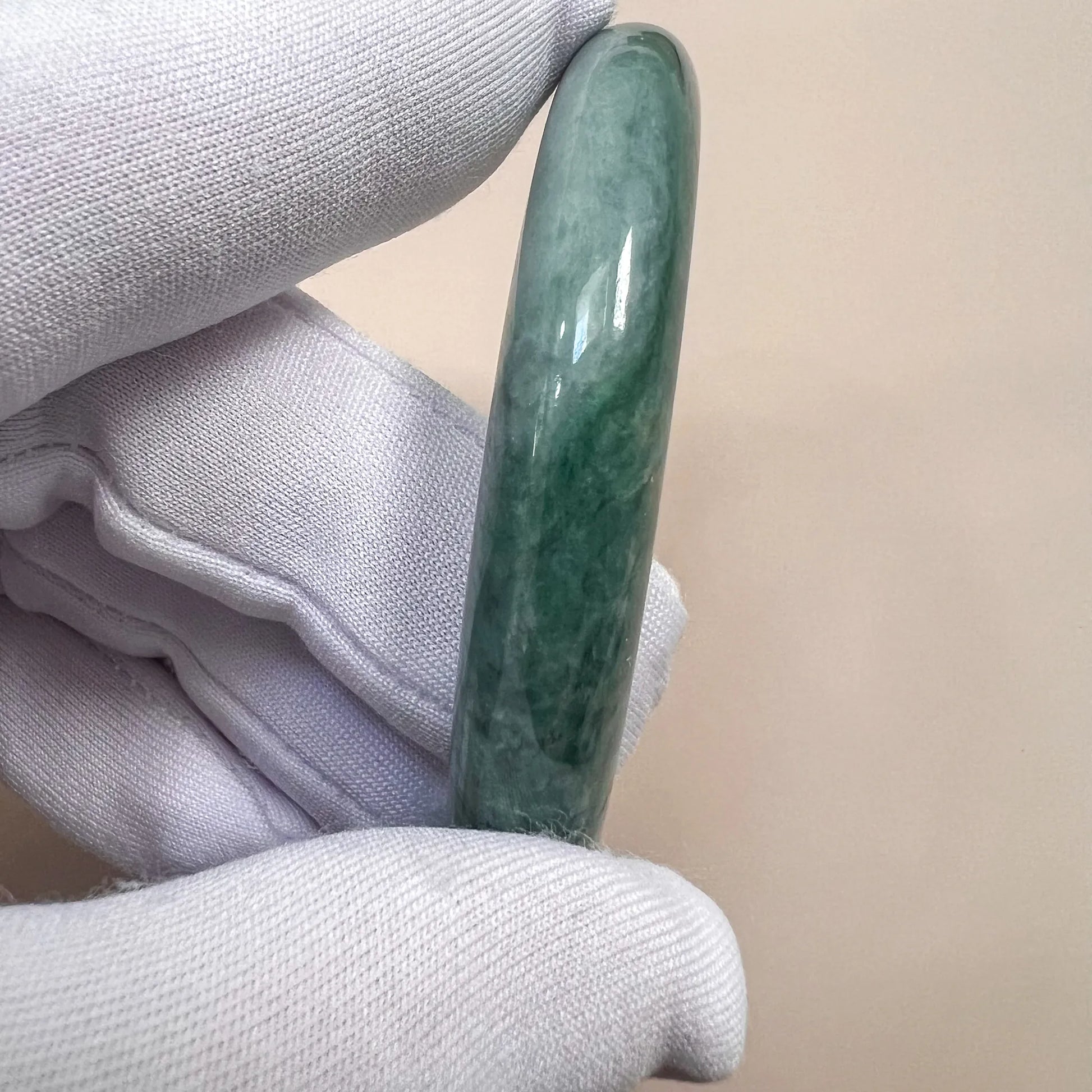 Side view of green jade bangle held in gloved hand, showing thickness and polished finish