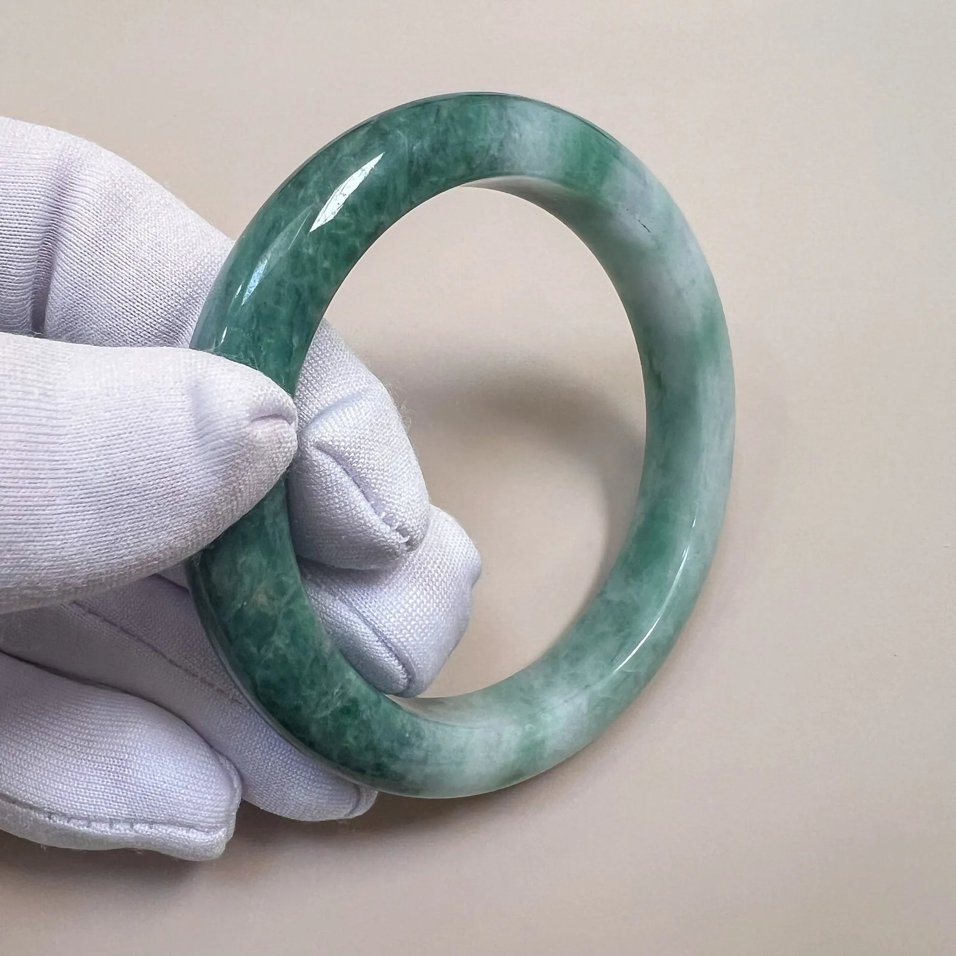 Close-up of mottled green jadeite bangle with glossy polished finish, held in white glove at an angle