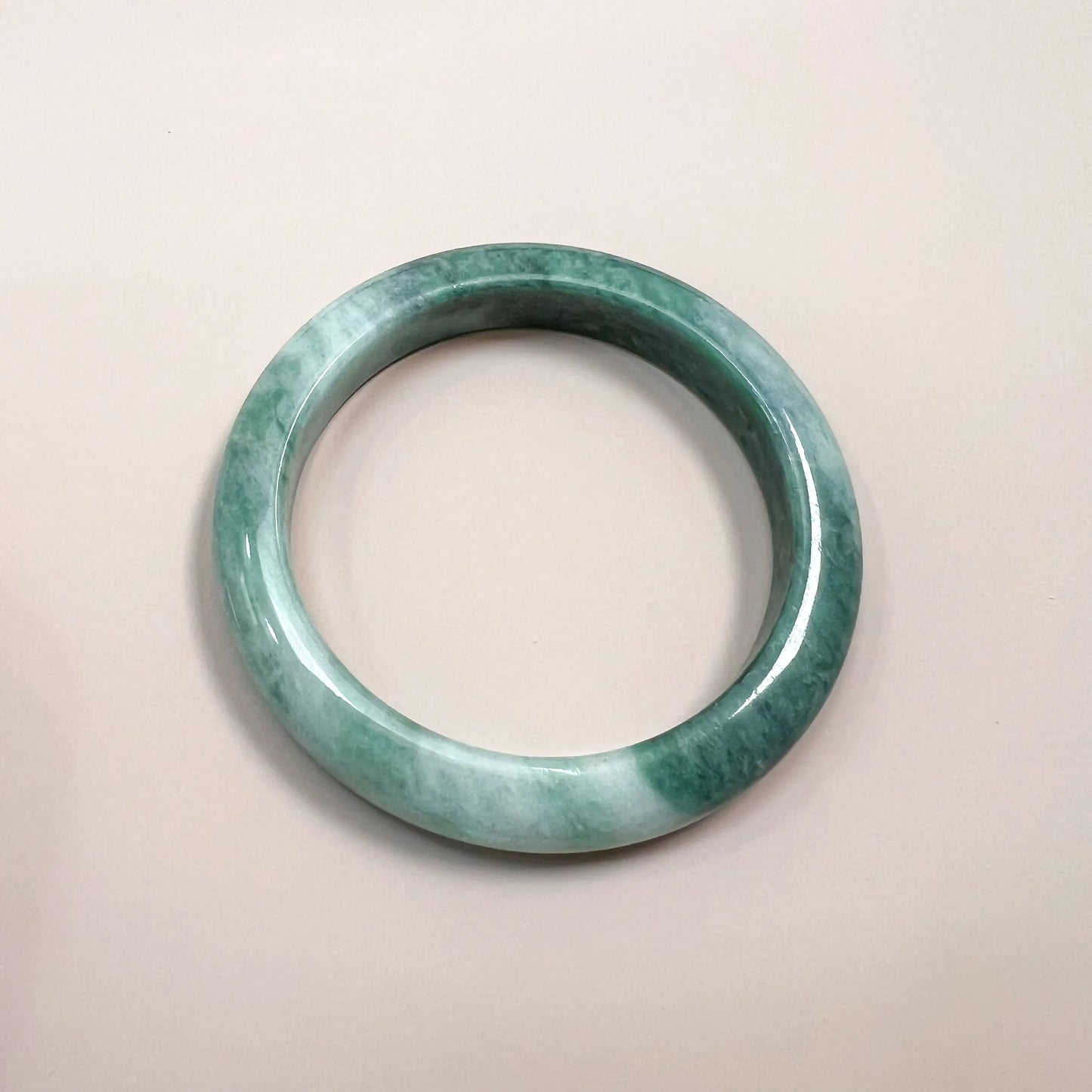 Top-down view of a mottled green jadeite bangle with glossy polished finish and smooth rounded profile