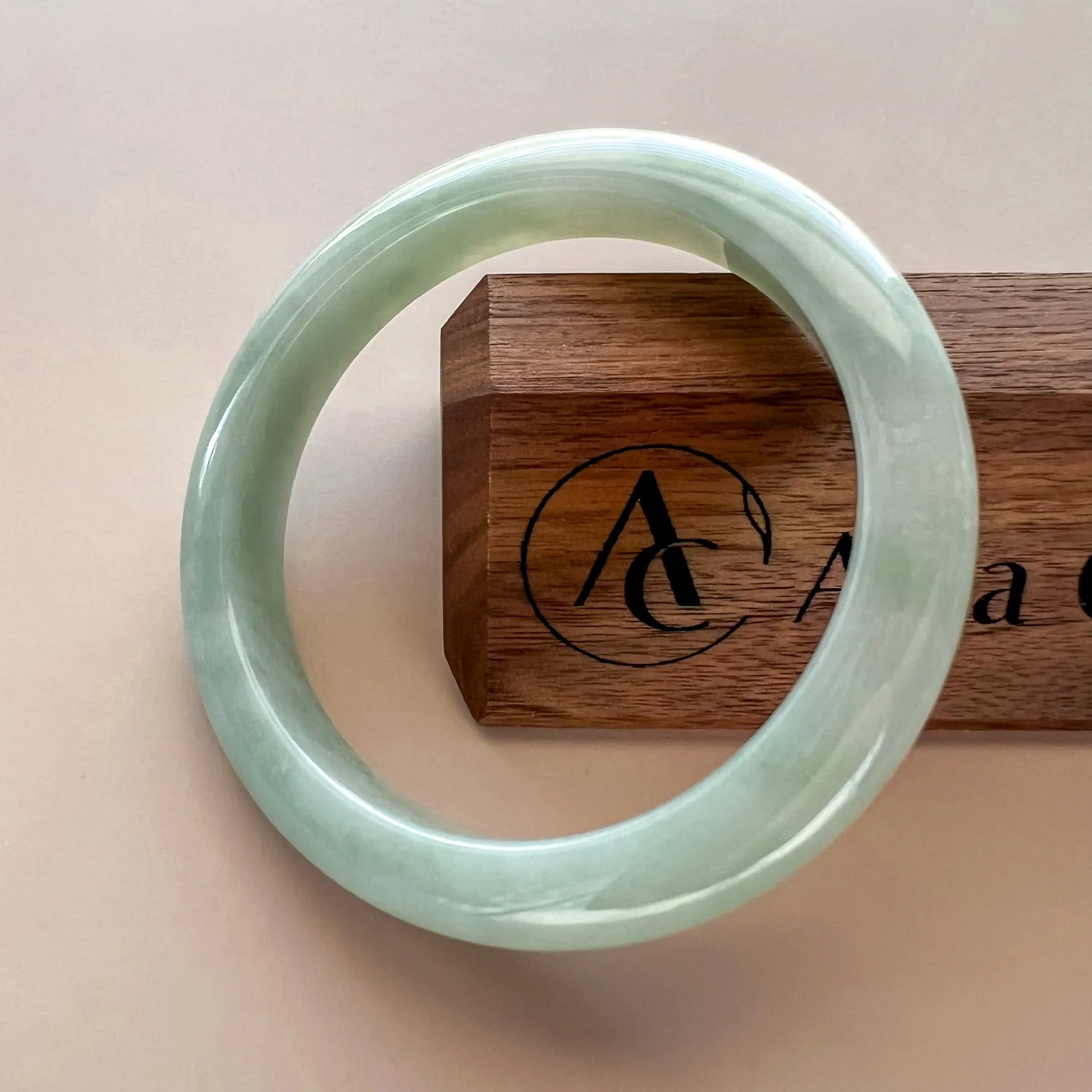 Front view of pale green jade bangle displayed on a wooden stand