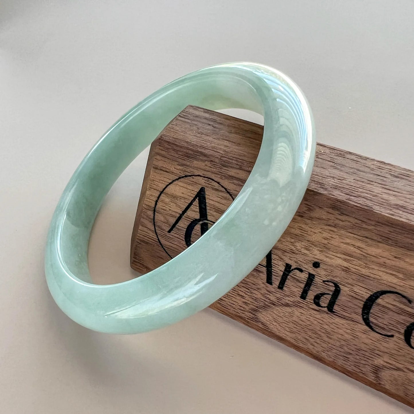 Angled view of polished light green jade bangle on branded wooden block