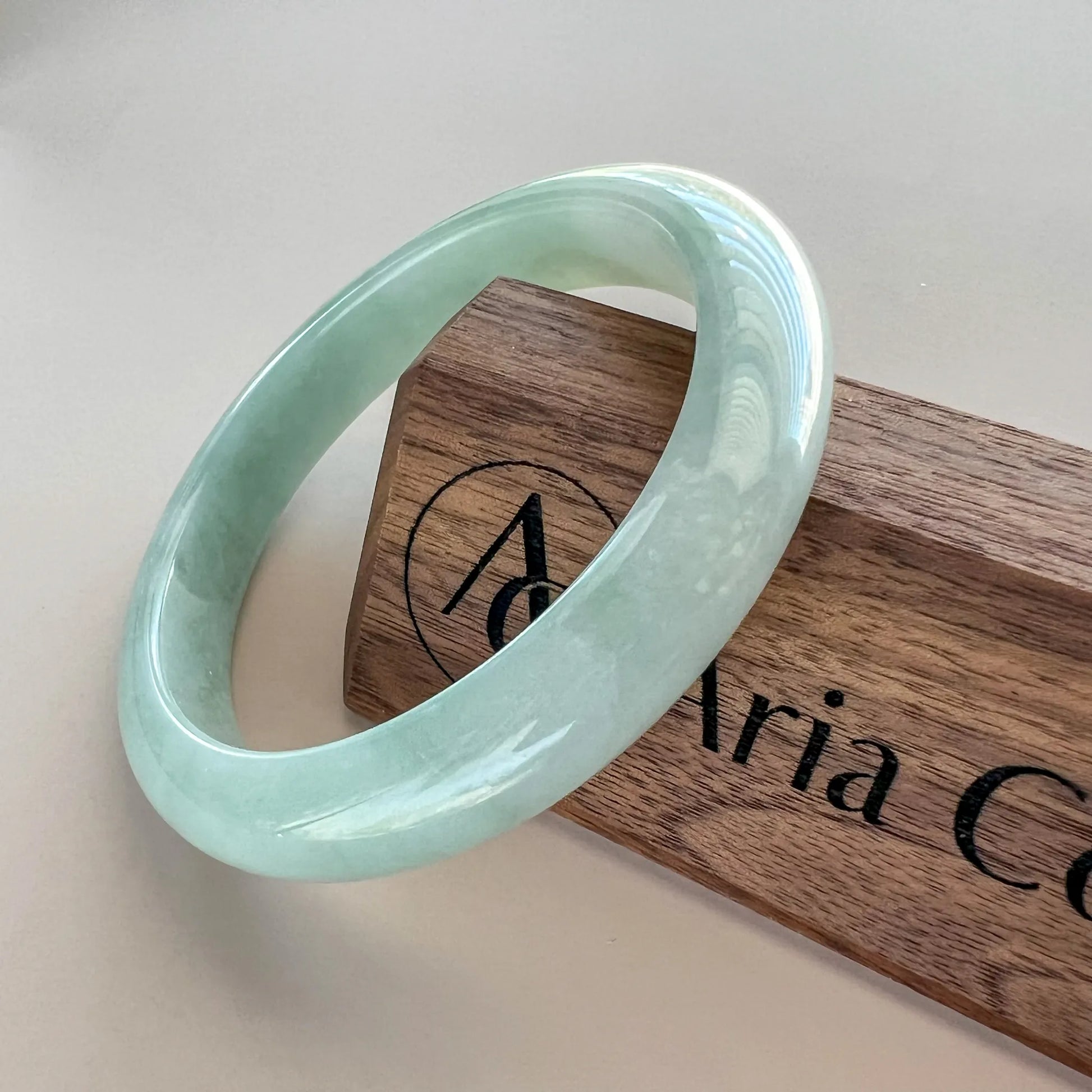 Angled view of polished light green jade bangle on branded wooden block