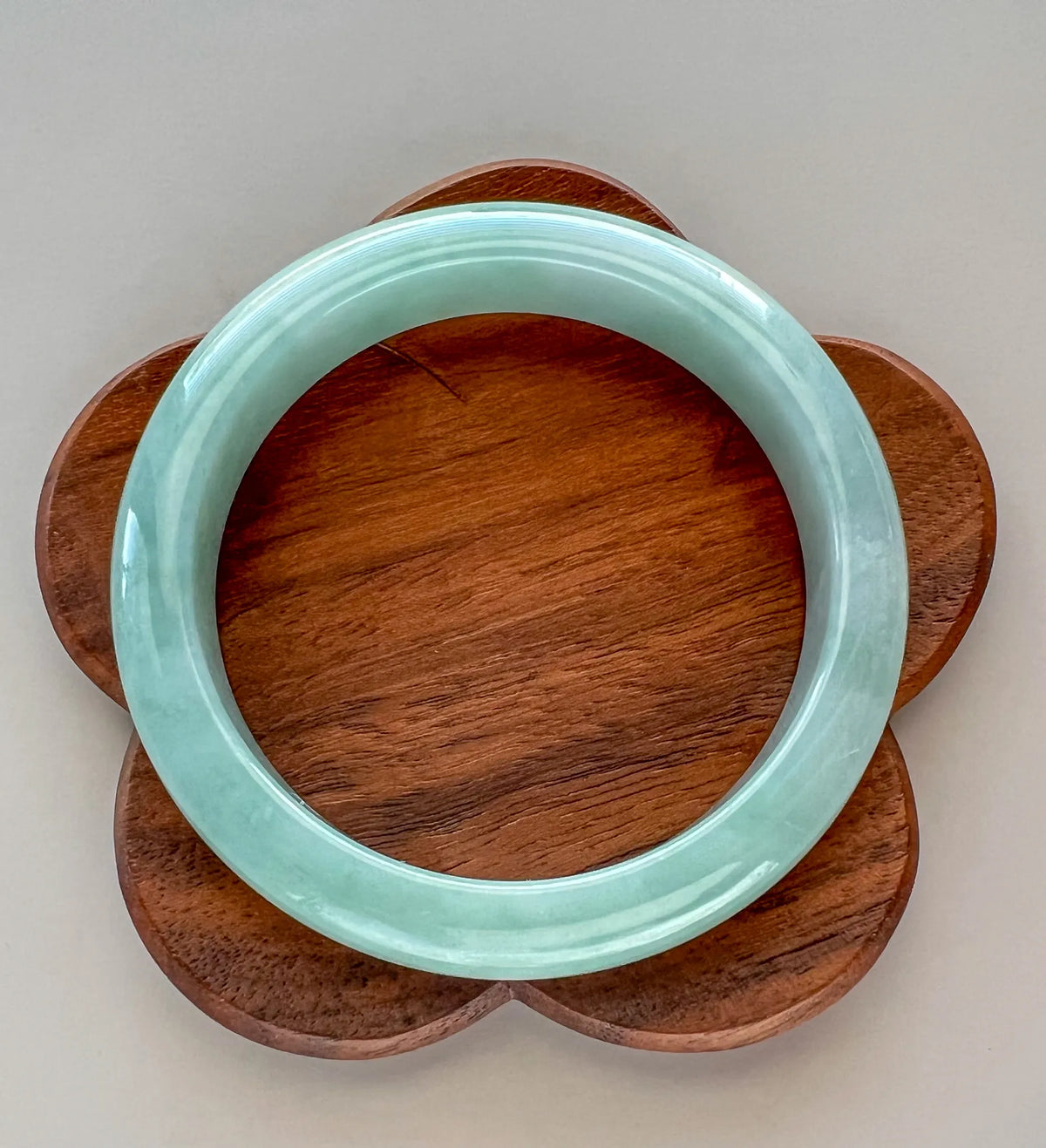 Top view of glossy light green jade bangle on flower-shaped wooden base