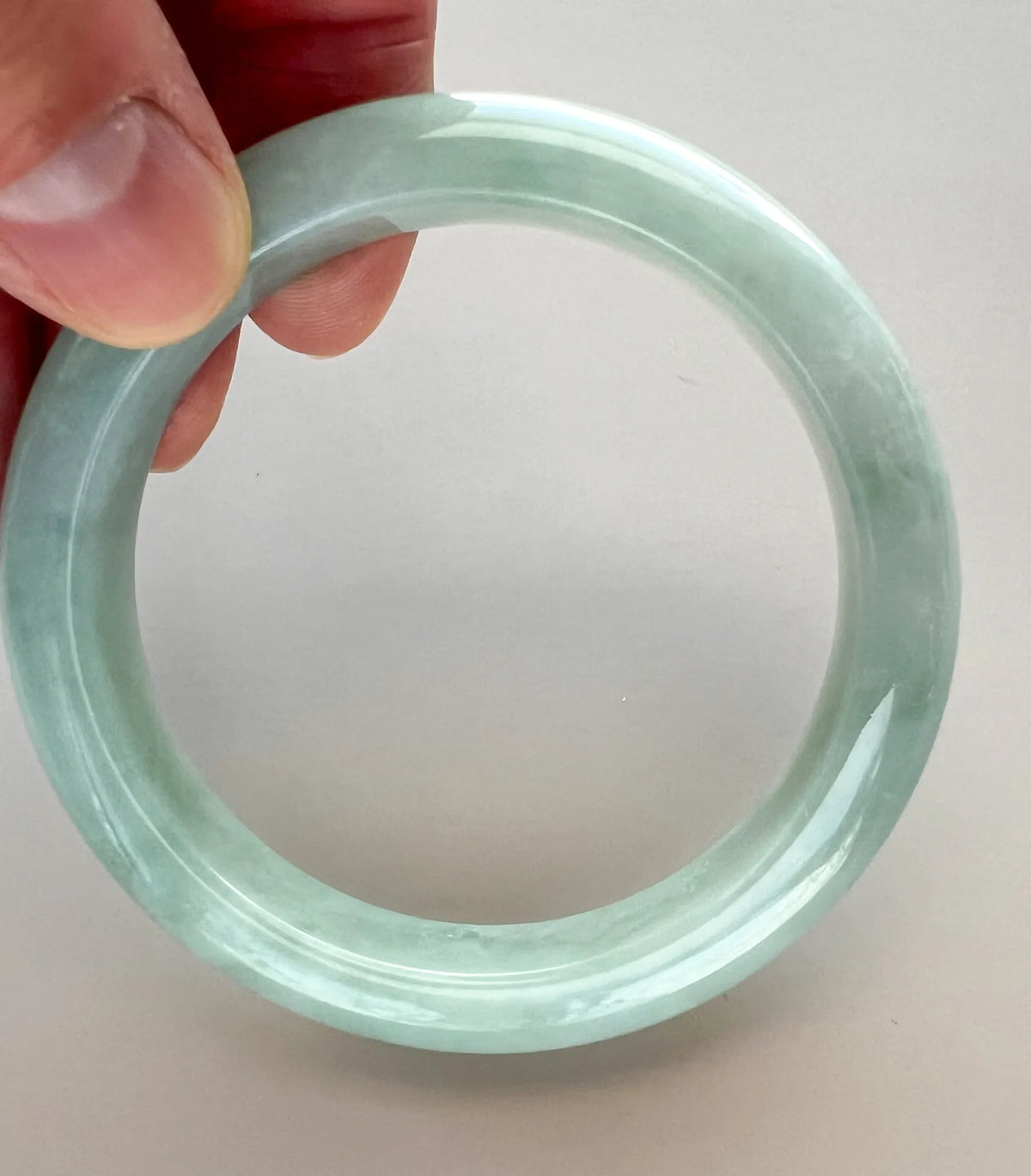 Angled view of the translucent green-blue jadeite bangle, showing its rounded profile and polished grooves