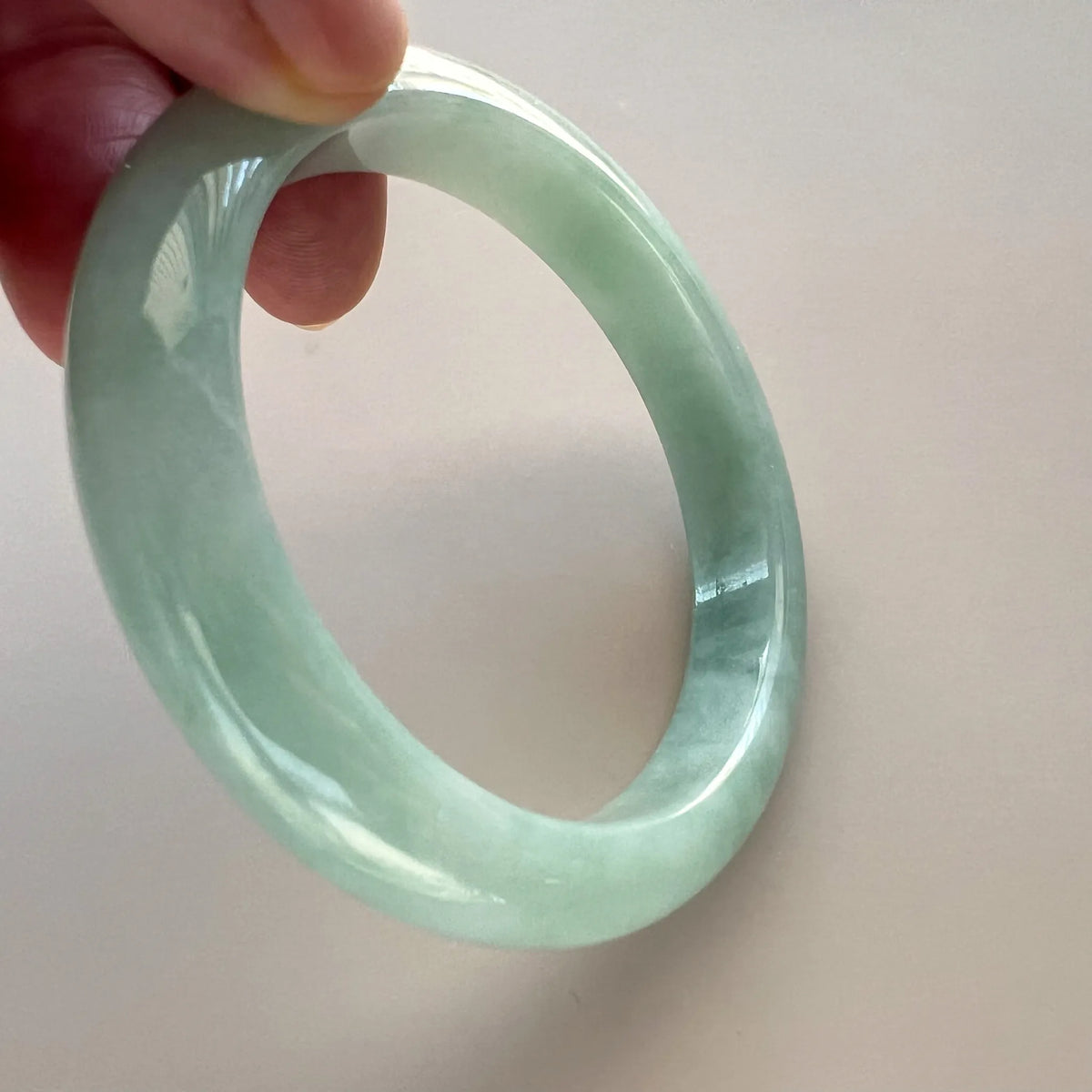 Side angle of polished light green jade bangle held by hand