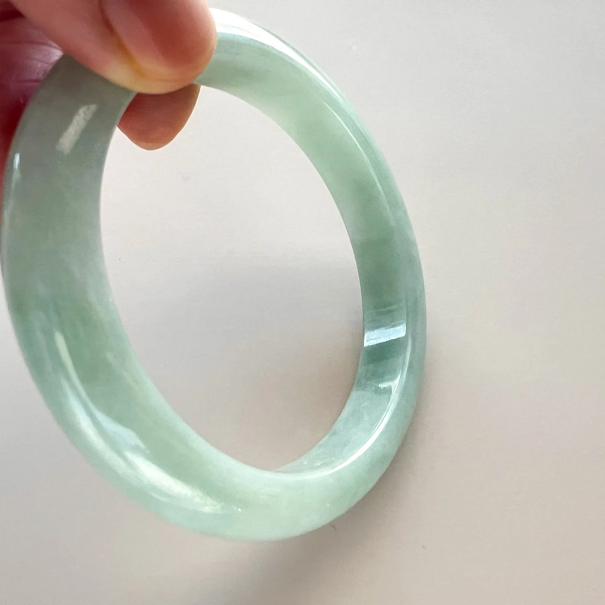 Diagonal hand-held view of smooth pale green jade bangle