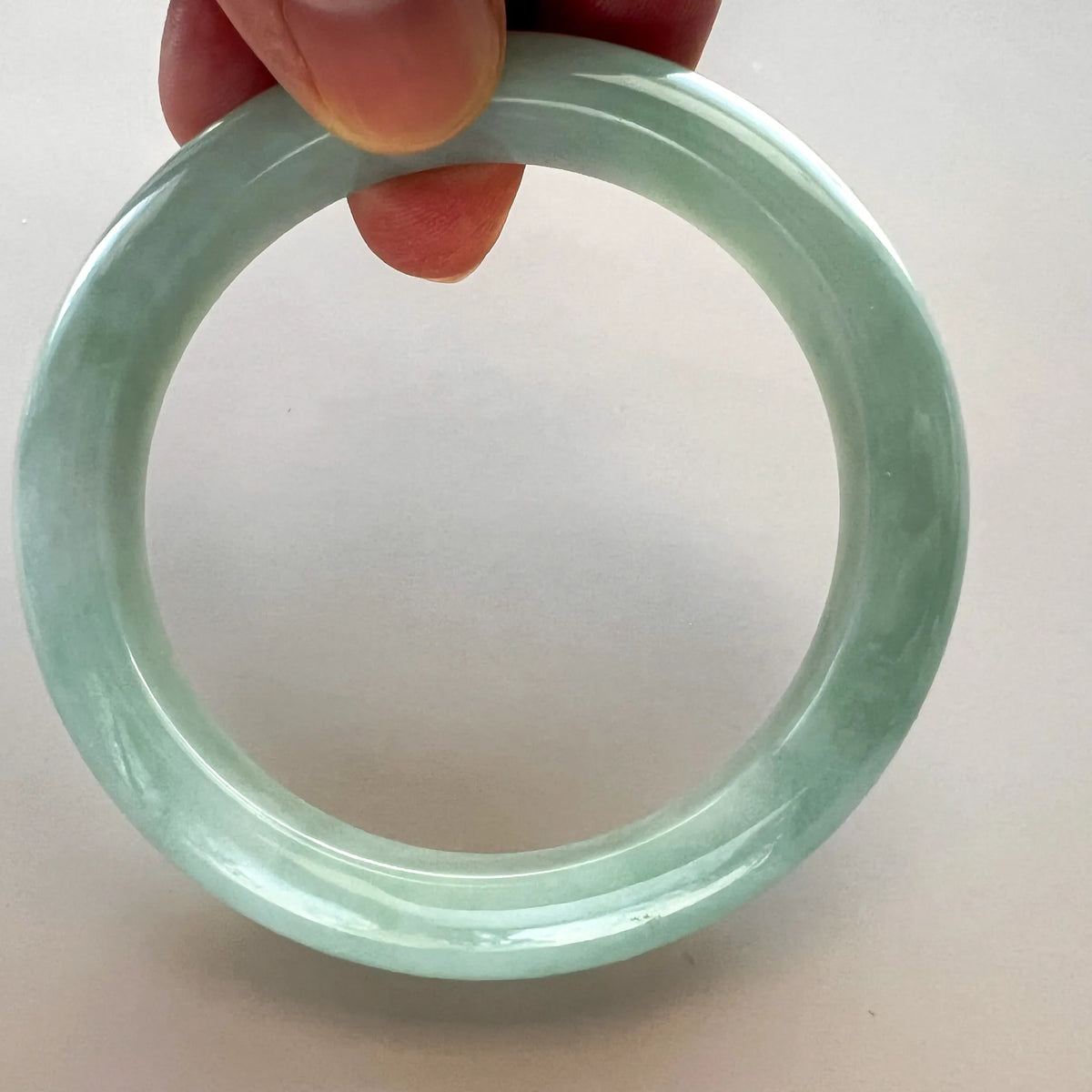 Close front view of glossy jade bangle held upright by hand