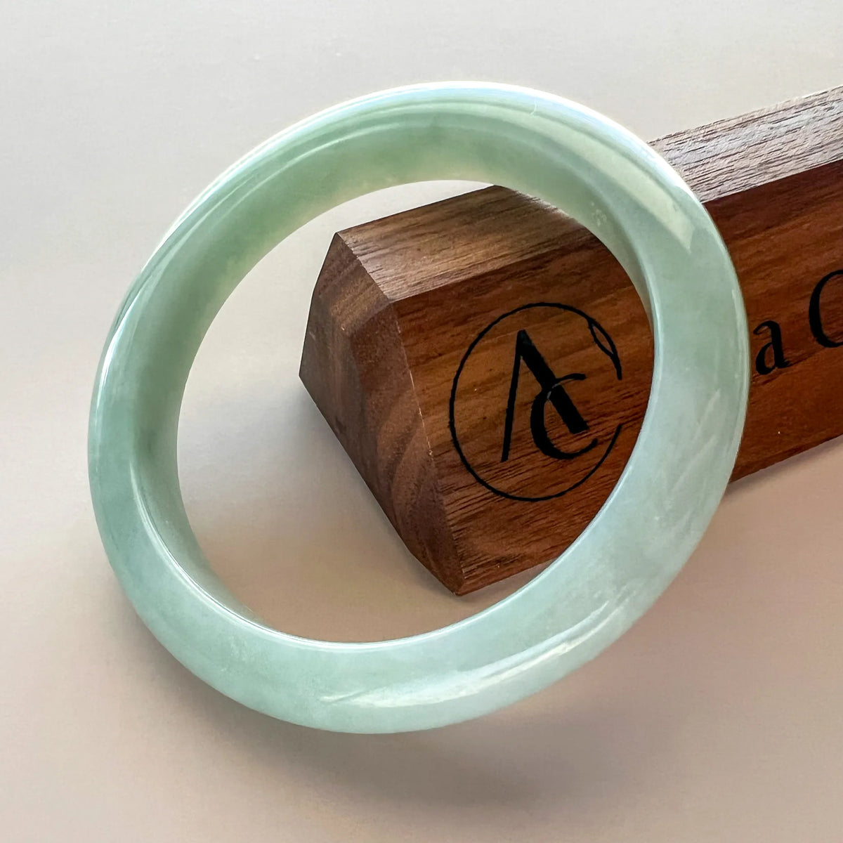 Light green Burmese Type A jadeite jade bangle, glossy polished finish, angled on wooden display block