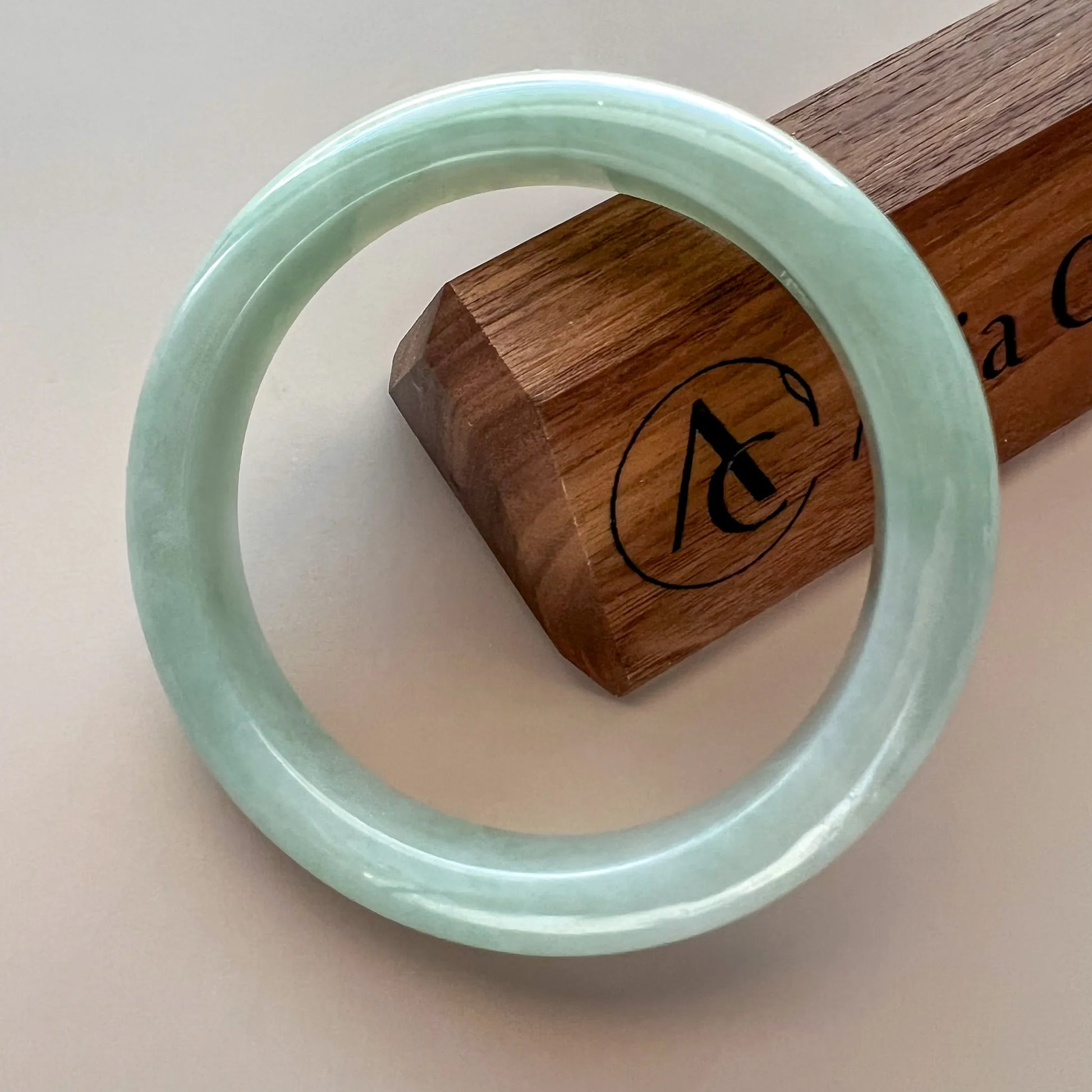 Light green Burmese Type A jadeite jade bangle, glossy polished finish, angled close-up on wooden box